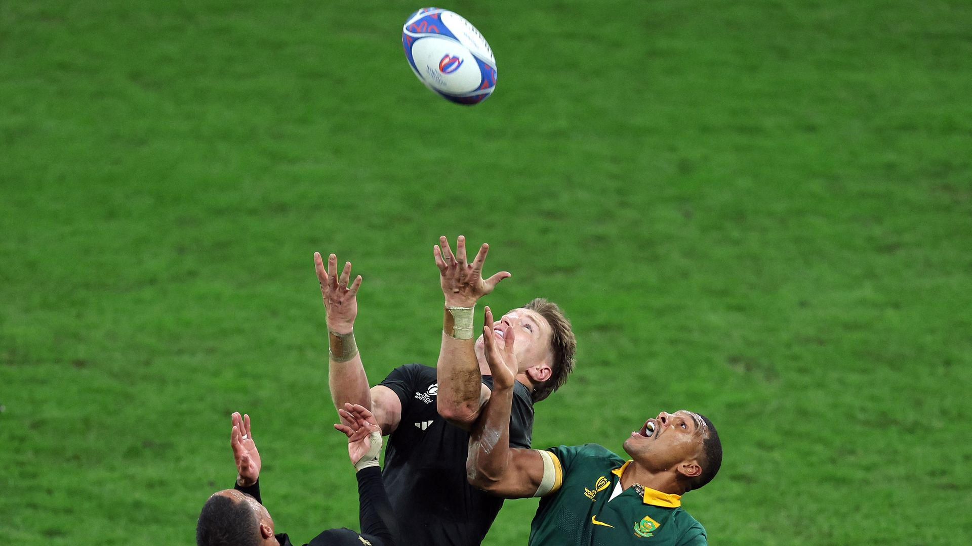 Rugby players in green and black jerseys leap for a ball.