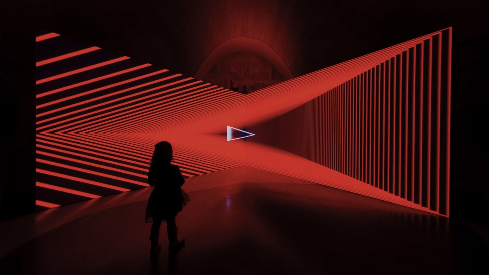 View of a red laser art installation with a girl standing in front of it.