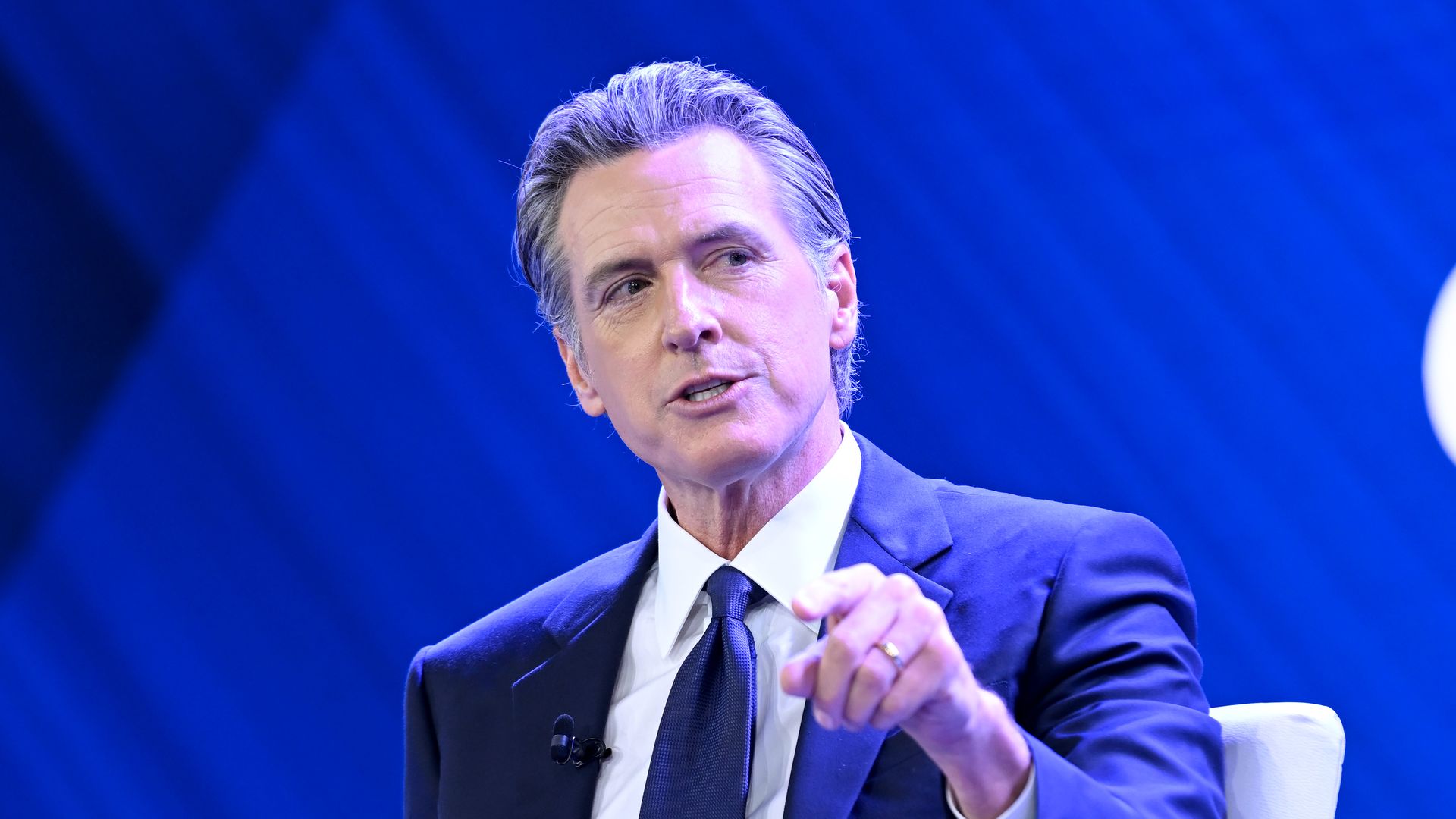 Photo of Gavin Newsom speaking while gesturing with his left hand on a stage