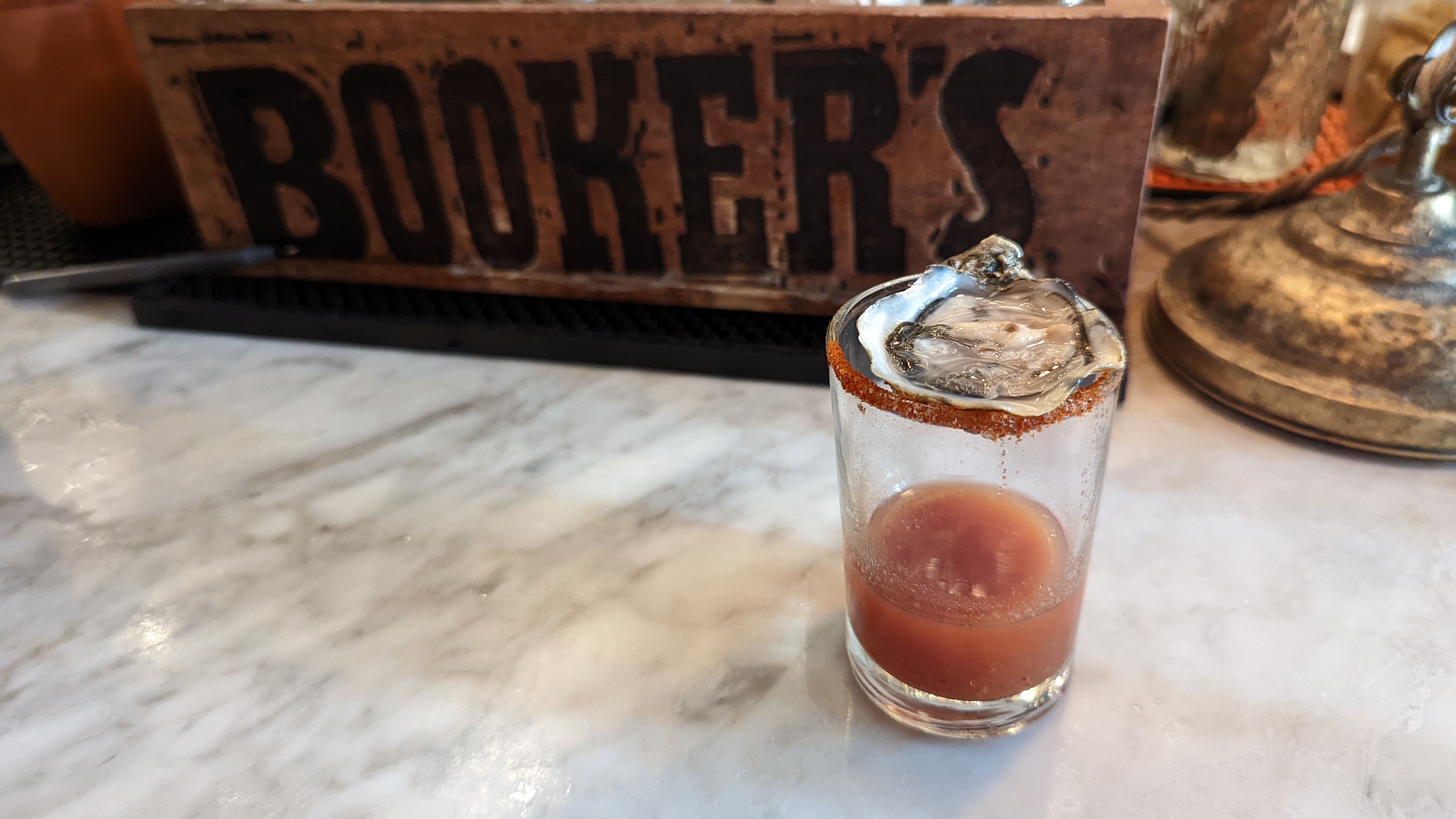 A shot glass of bloody mary mix with an oyster on top.