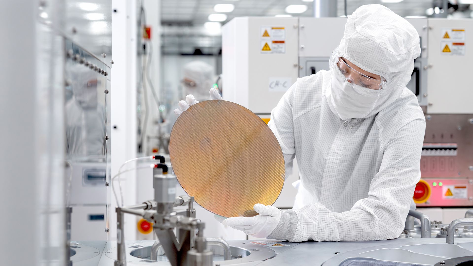 A person with white protective gear holds a thin disk in a lab