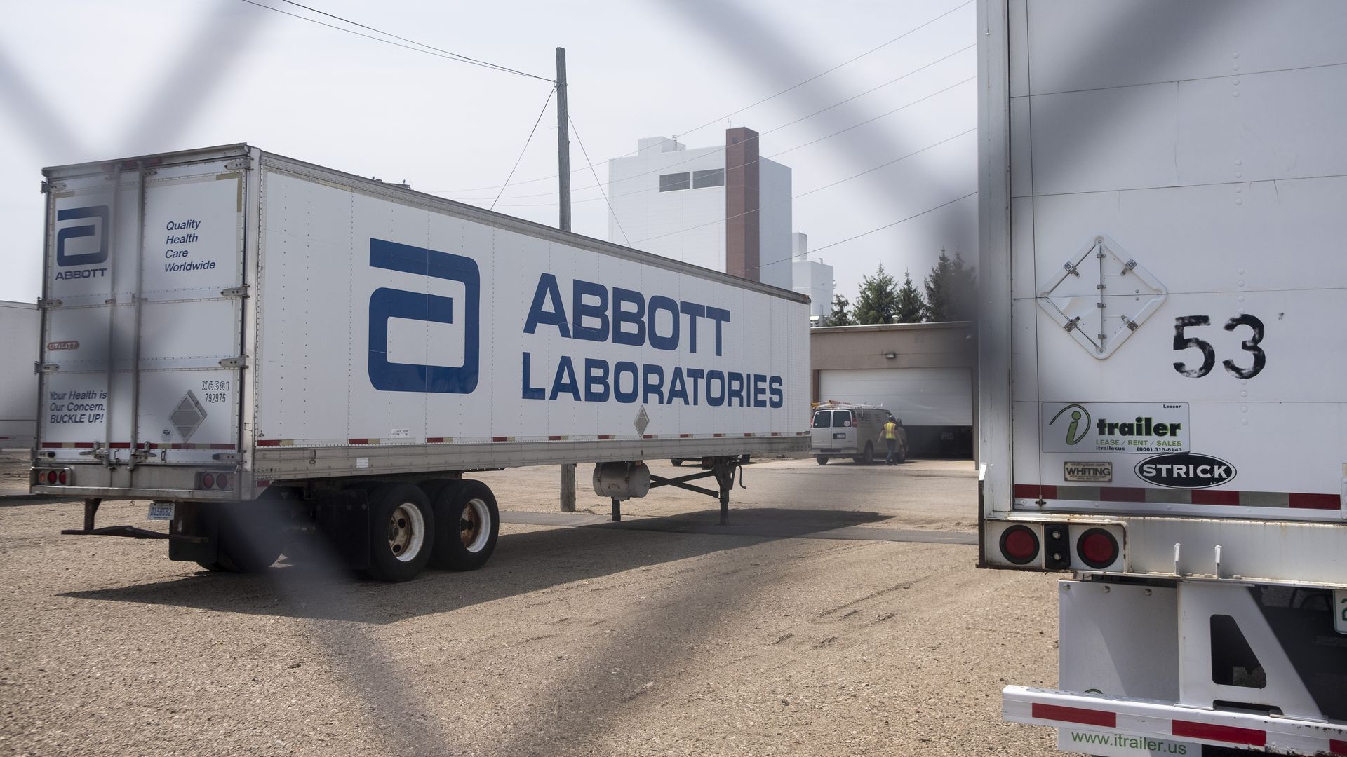 Photo of a truck trailer with the Abbott Laboratories' name and logo printed on the side, as viewed through a wire fence