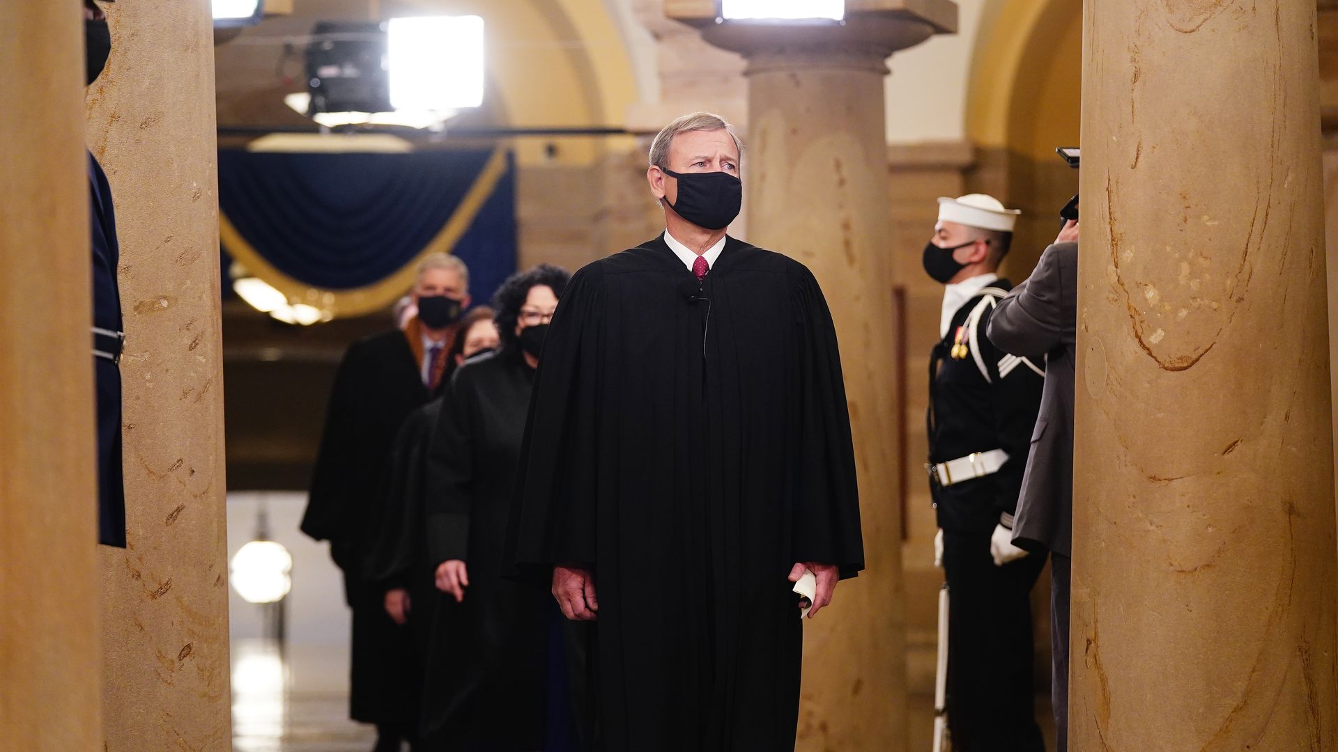 Photo of a masked John Roberts in his black Supreme Court robe walking in the crypt of the U.S. Capitol with other justices behind him