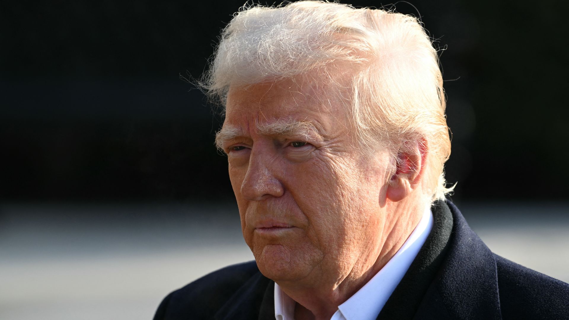 Man in suit and coat pictured from shoulders up squinting with mouth closed