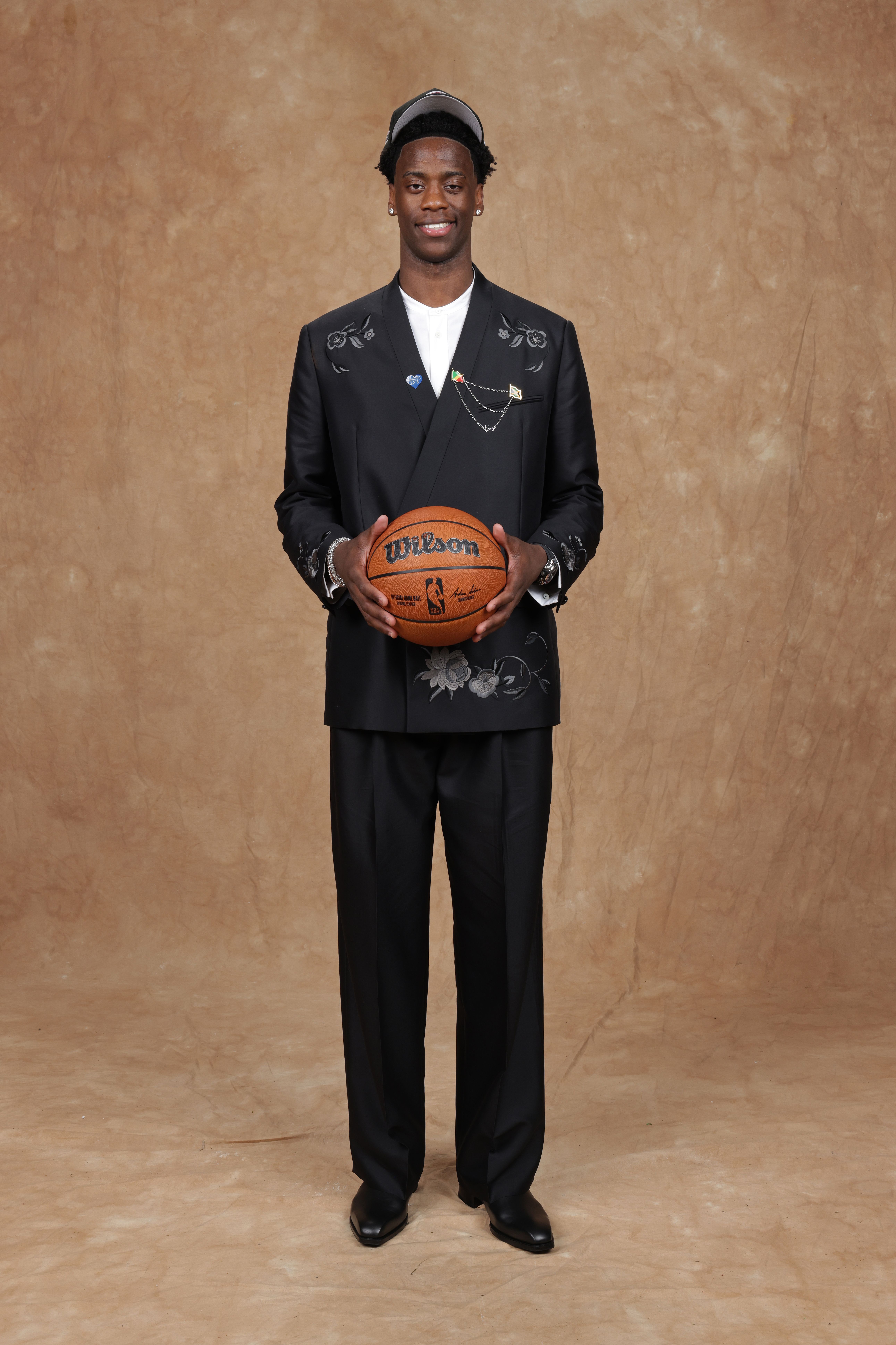 AJ Dybantsa in a suit stands tall and holds a basketball in his hand for a picture