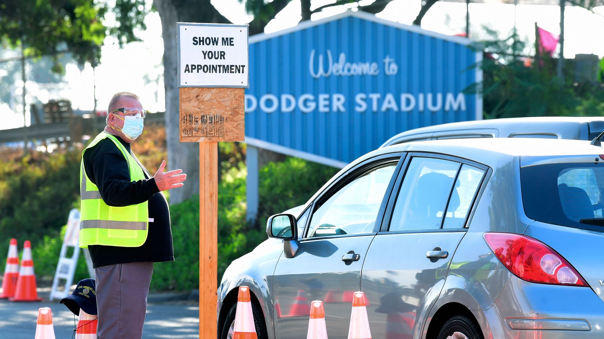 A health worker volunteer wearing a facemask and eye protection checks for appointments from arrivals for Covid-19 testing at Dodger Stadium in Los Angeles, California