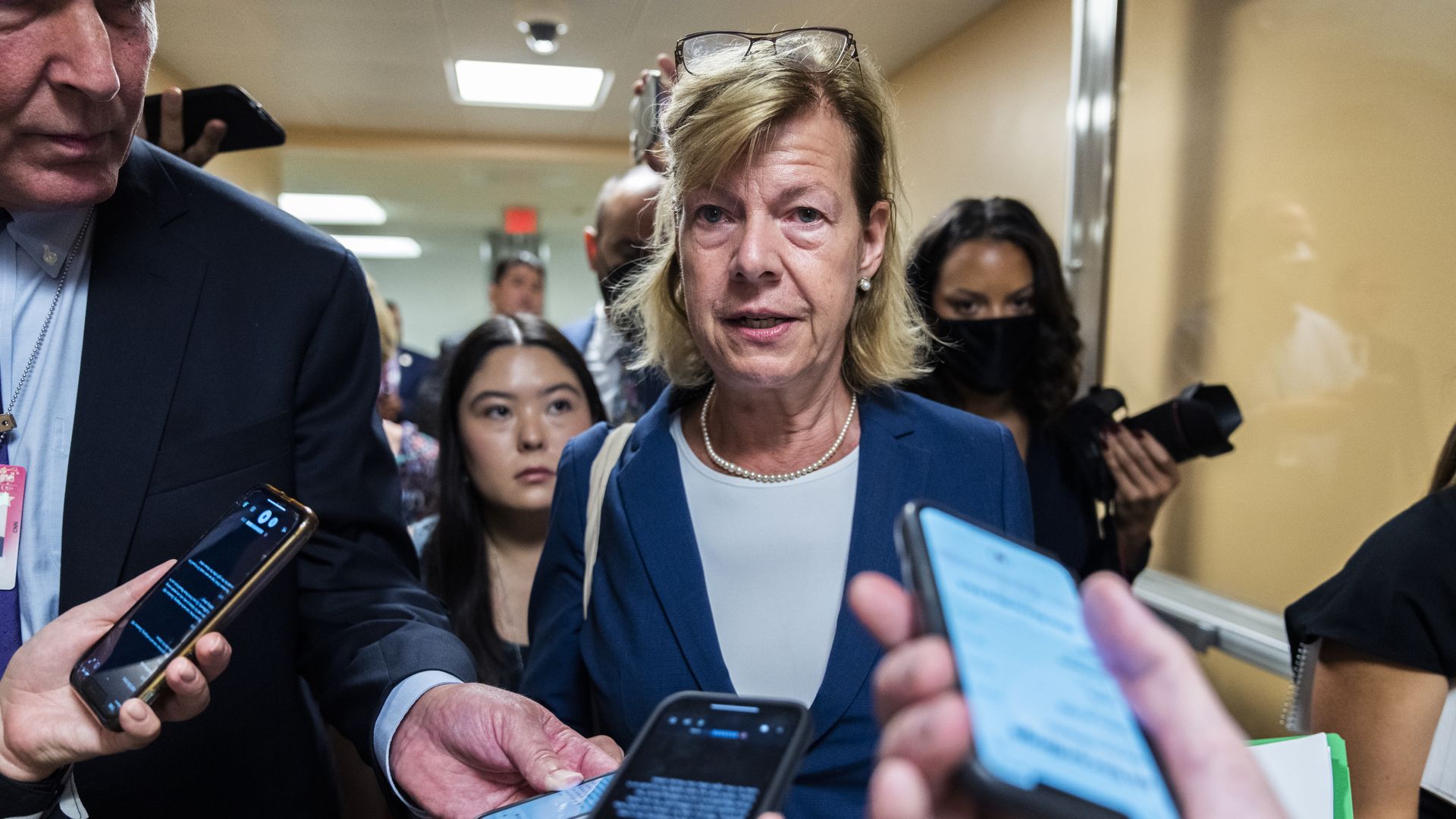 Sen. Tammy Baldwin, wearing a blue jacket, speaks to reporters in the Capitol basement.