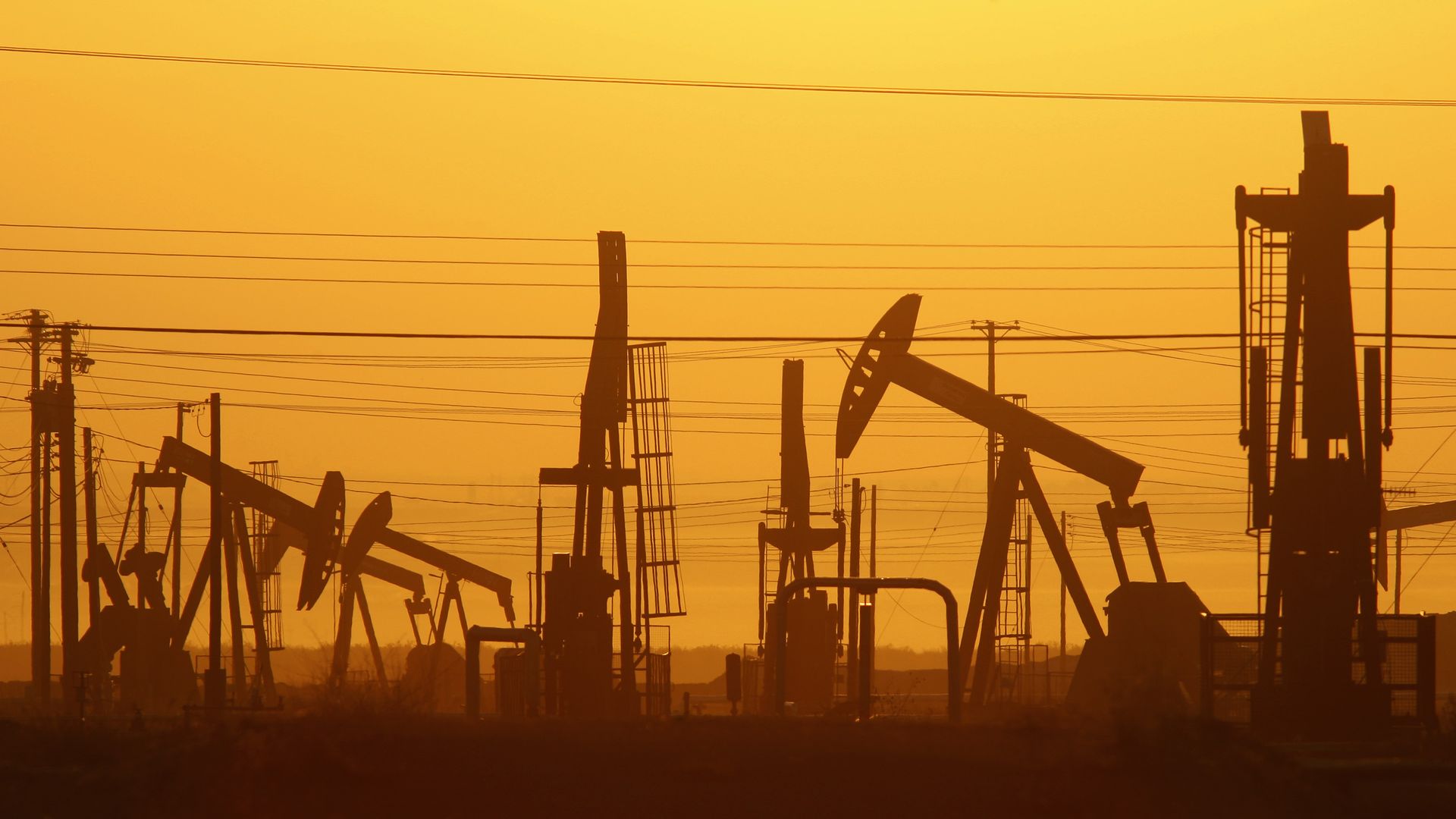 A silhouette of oil pump jacks against an orange sky.