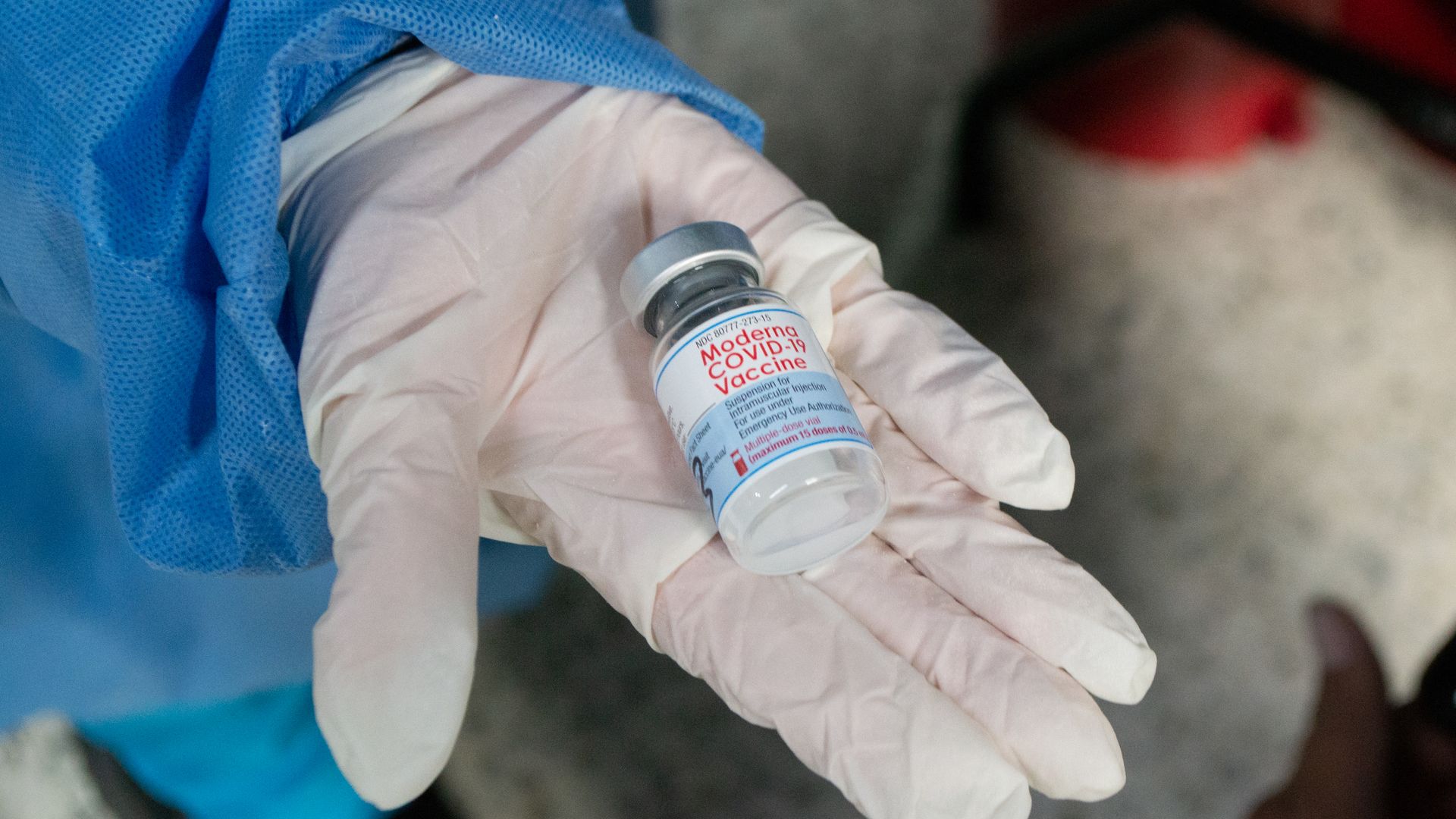 Picture of a hand wearing a surgical glove holding a Moderna vaccine vial