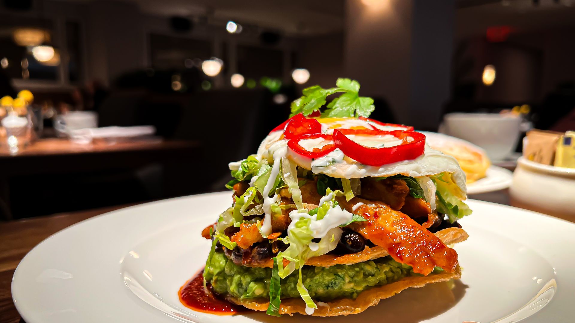 A stack of crispy tortillas layered with guacamole, chicken and a fried egg. 