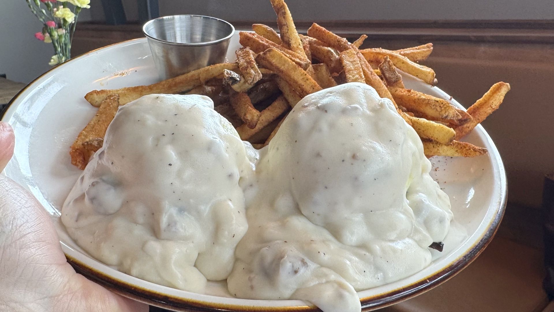 A plate of biscuits covered in gravy with a side of french fries. 