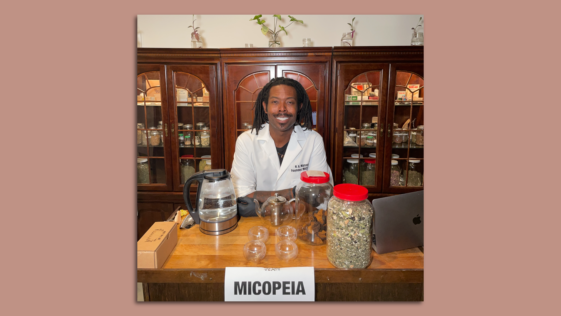 Massey standing with products in front of him, in front of a set of shelves.