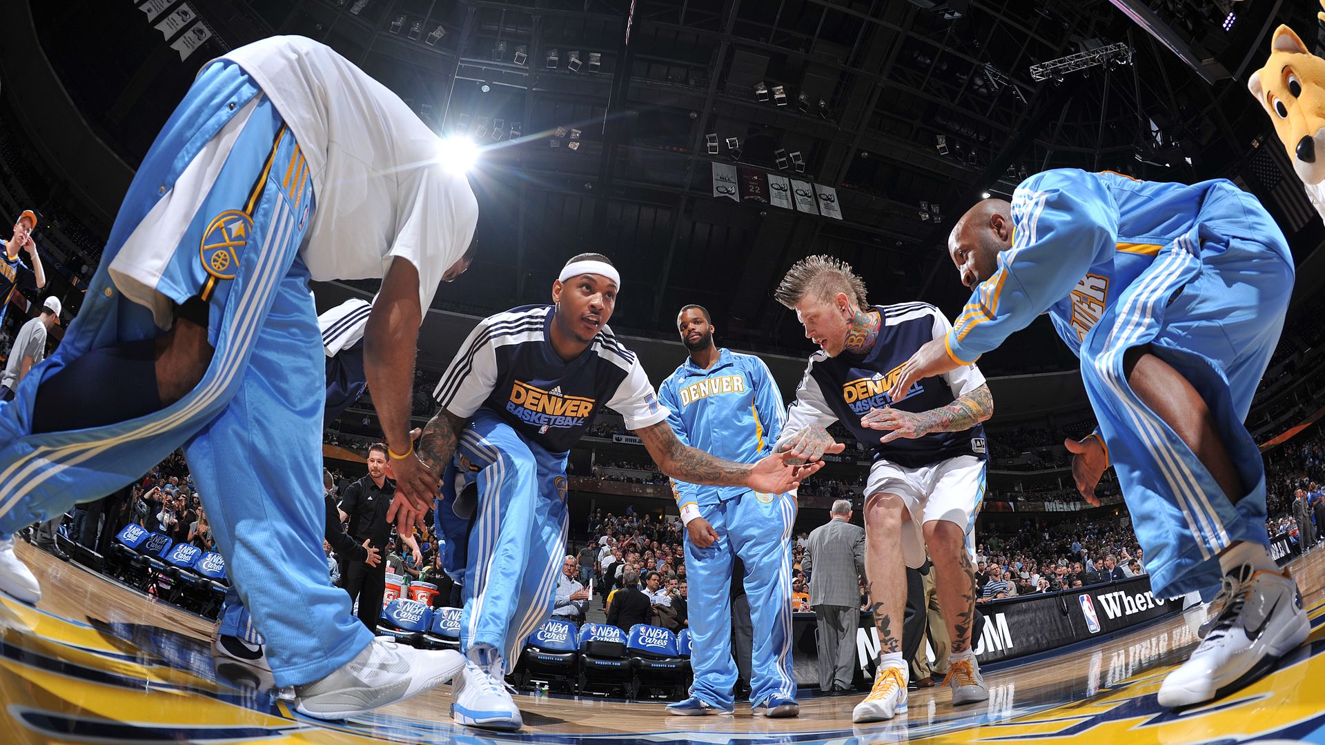A man crouches down to high-five teammates surrounding him on a basketball court. 