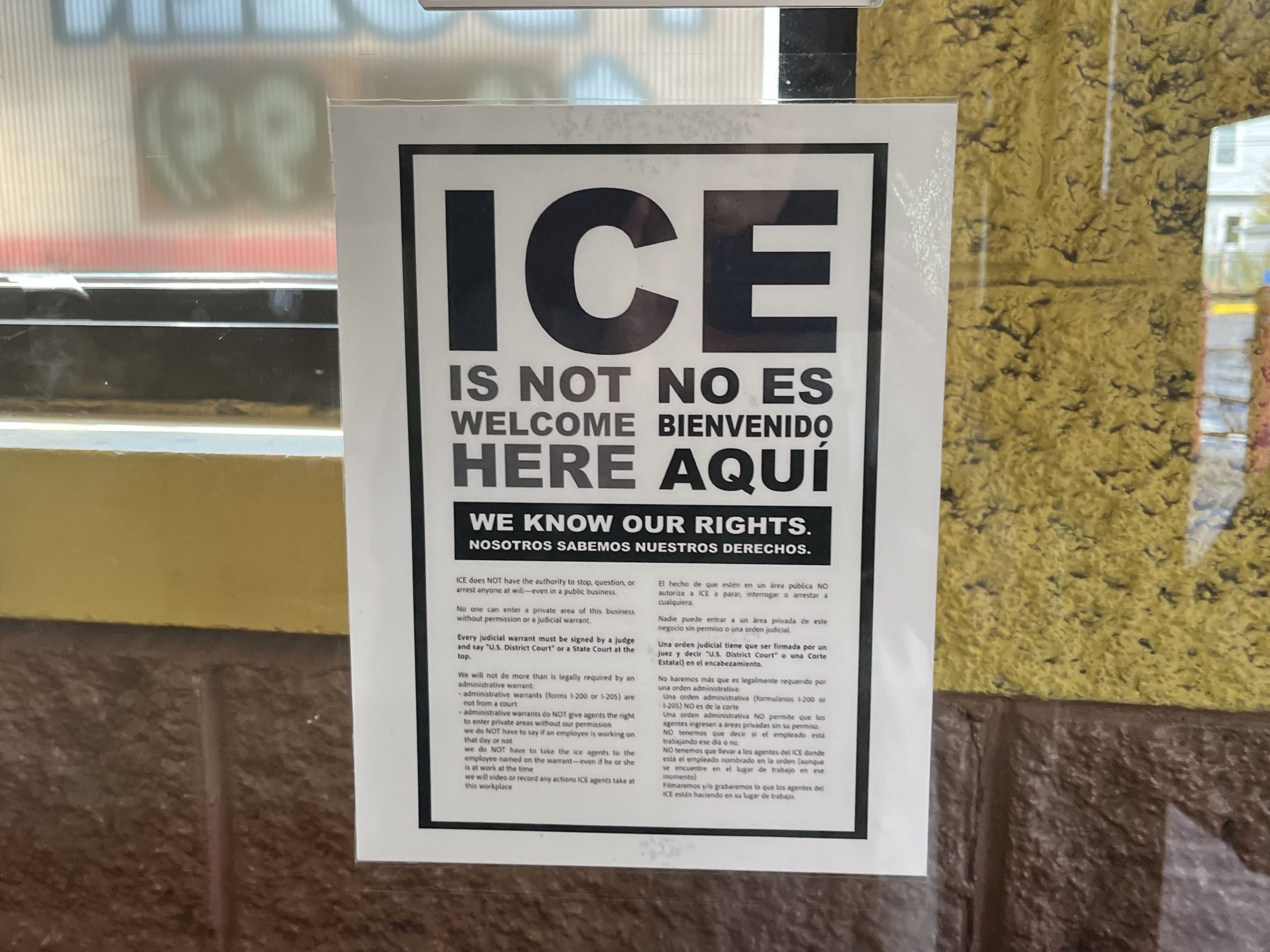 Poster on window with text in English and Spanish stating ICE is not welcome here, we know our rights, and explaining legal rights about ICE authority and warrants.