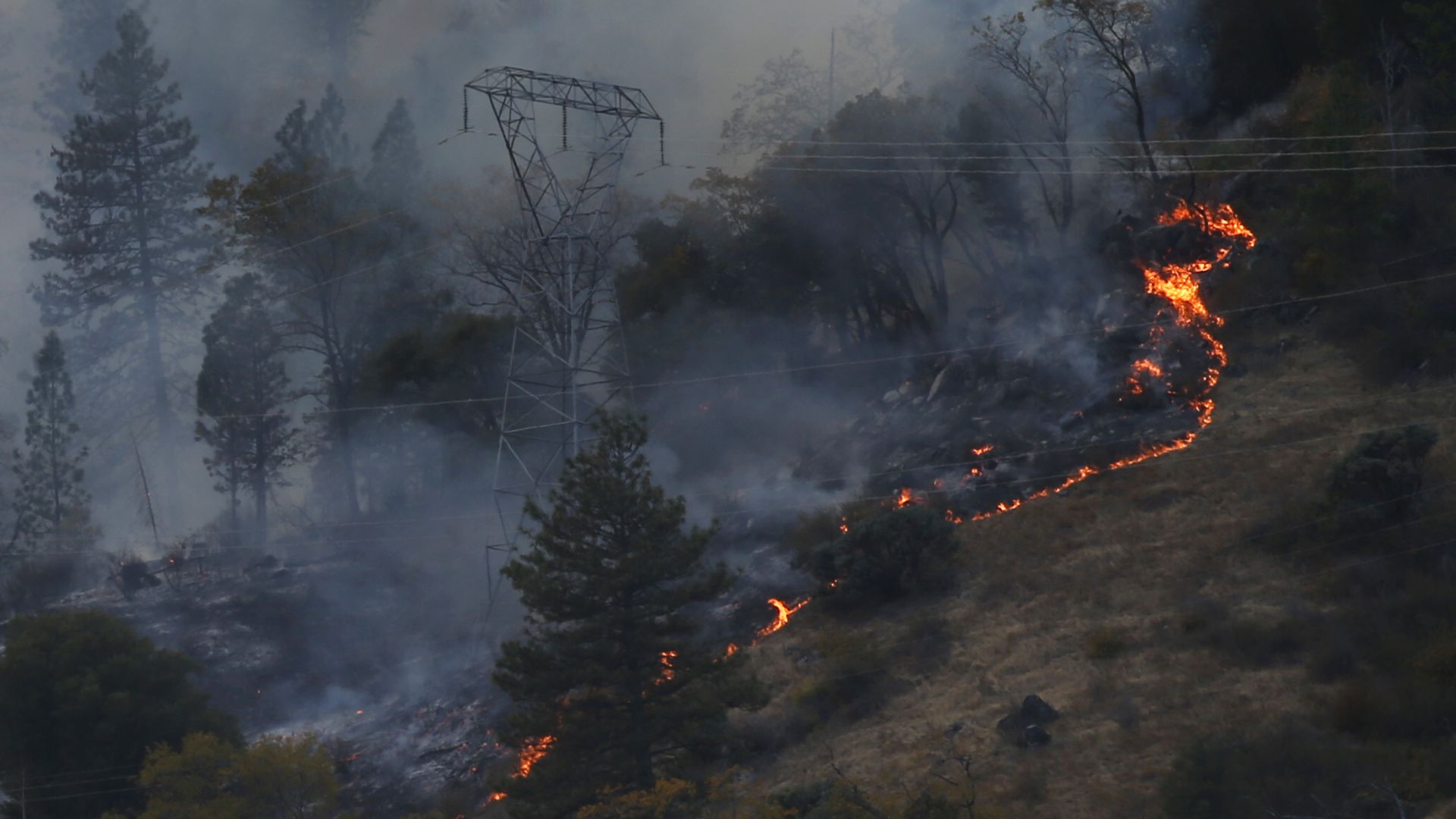 Photo of a transmission tower with a wildfire nearby