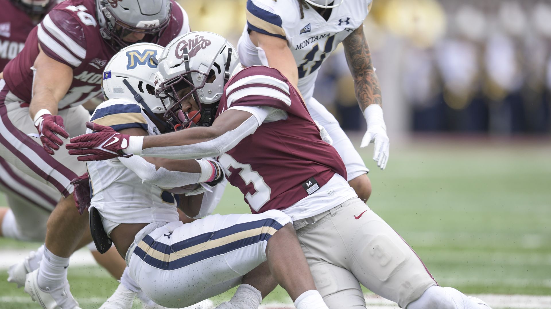 Two football players embrace as they fall to the ground in a tackle.
