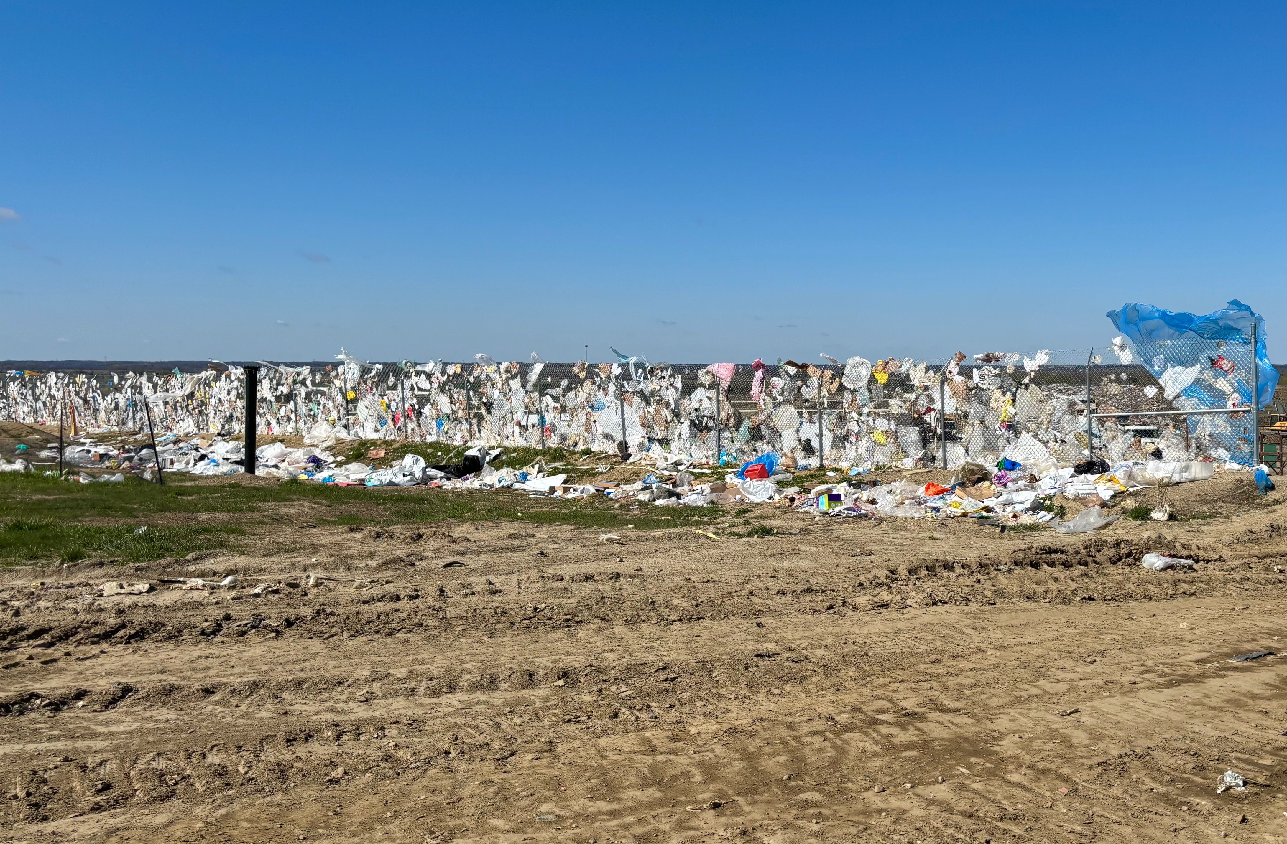 A chain-link litter fence covered with plastic bags and other floating trash on a windy day