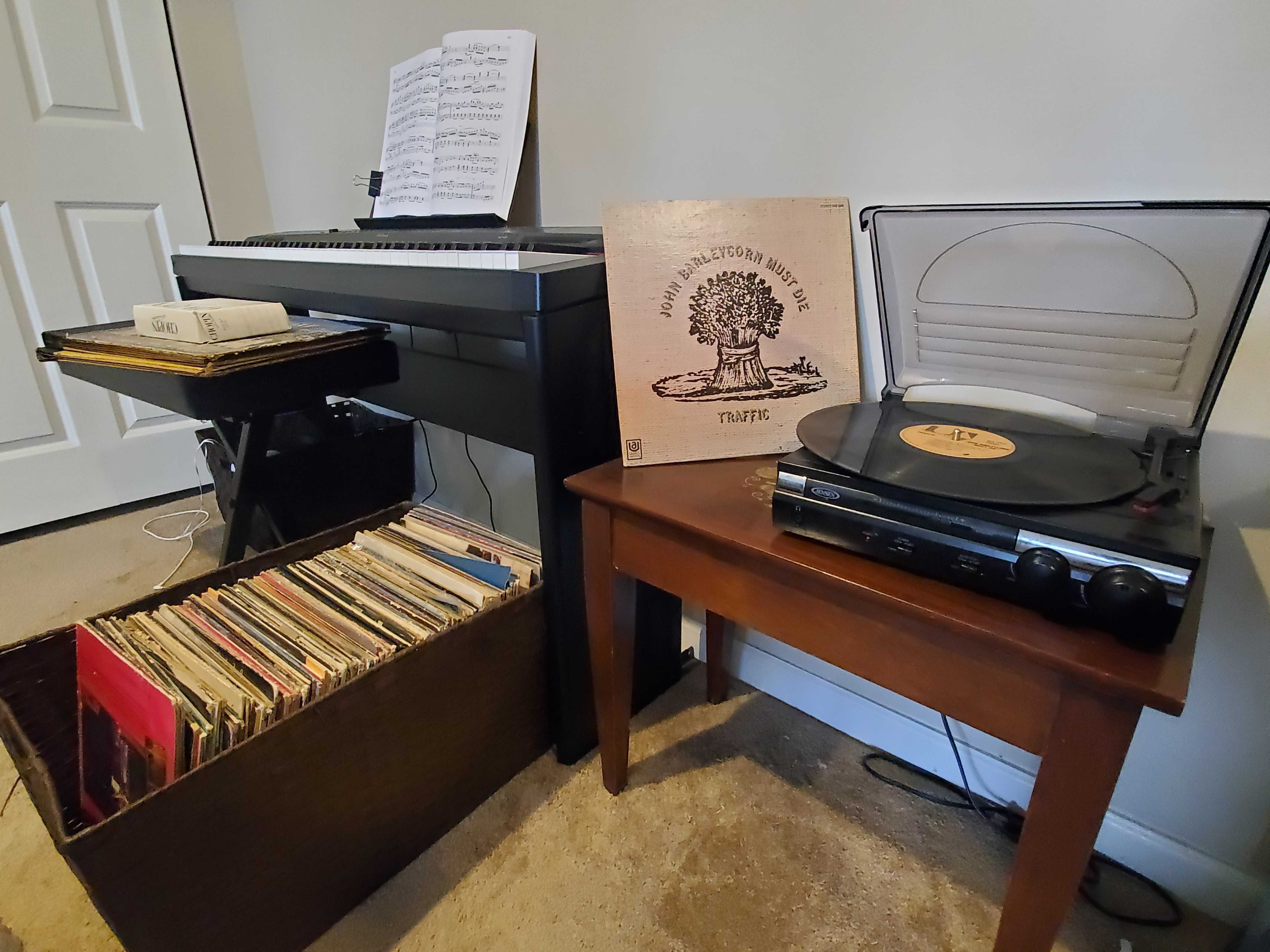 A record player with a stack of vinyls next to a piano.