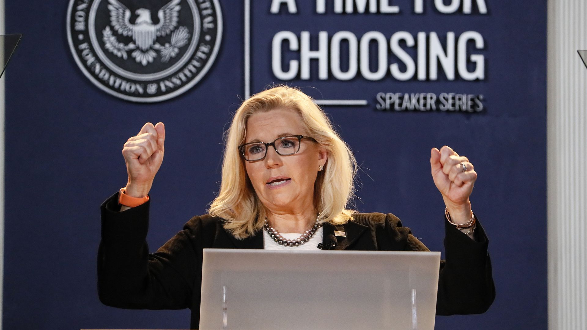 Rep. Liz Cheney (R-Wyo.) wearing a black blazer, white shirt and glasses, raises her arms during a speech at the Ronald Reagan Presidential Foundation & Institute.
