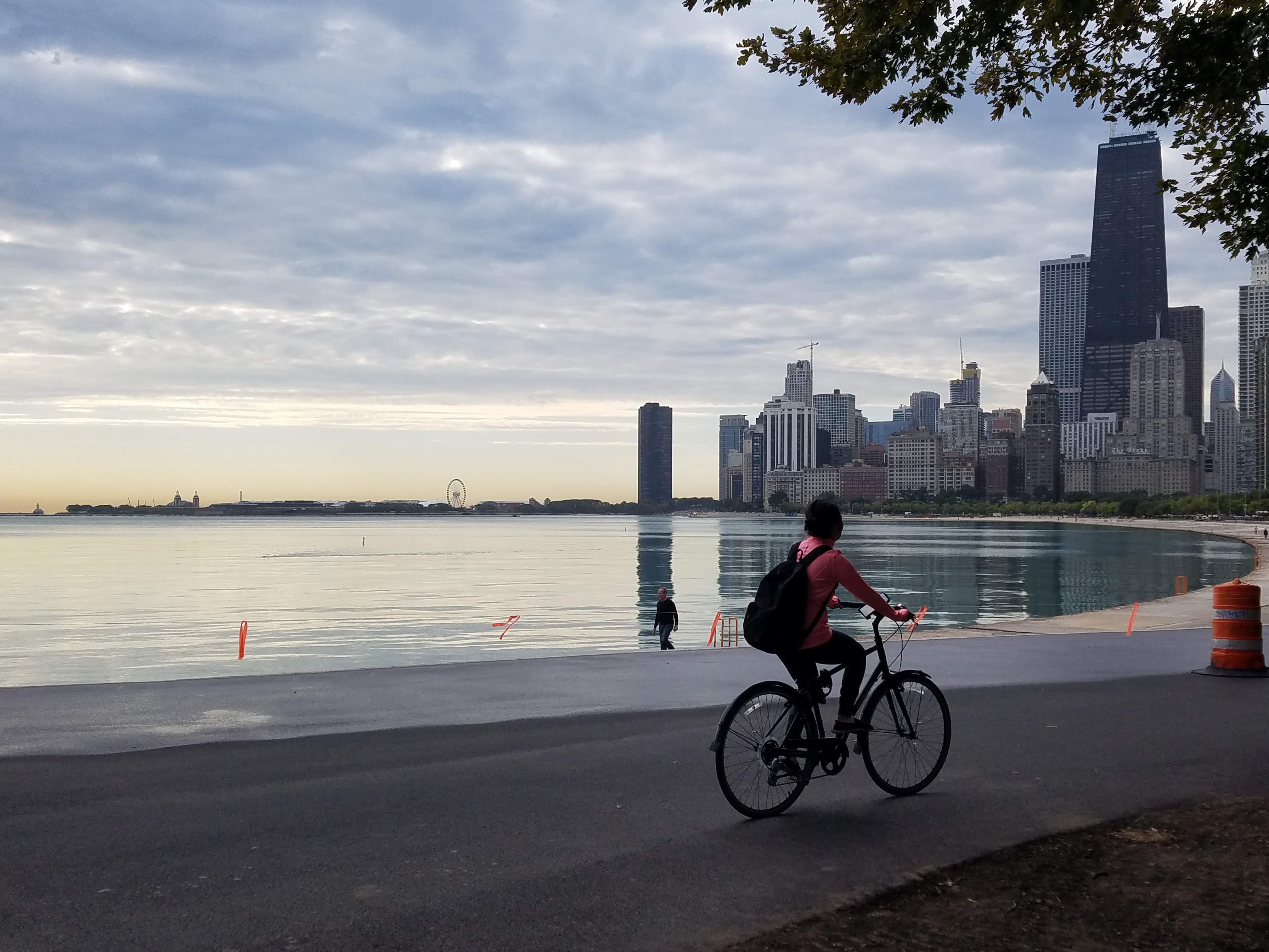 Photo of a man riding a bicycle by a lake and skyscrapers.
