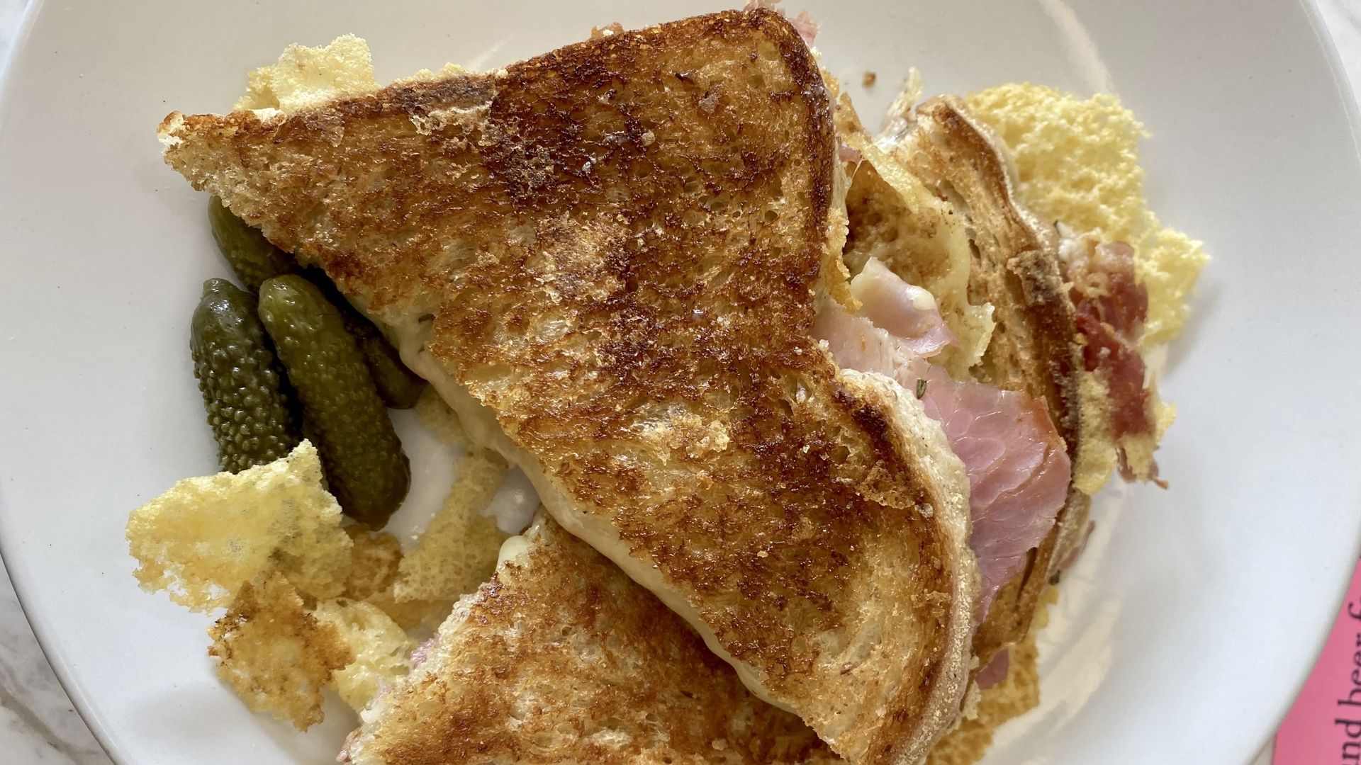 A picture of a grilled cheese sliced diagonally with some Virginia ham on a white plate.