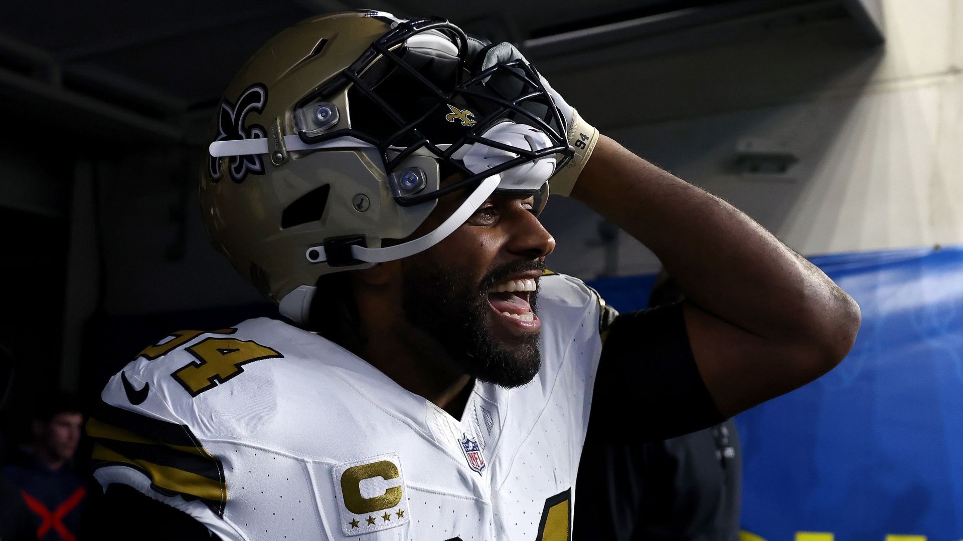 Cam Jordan lifts his Saints helmet and shouts as he enters a football stadium through the players' tunnel.