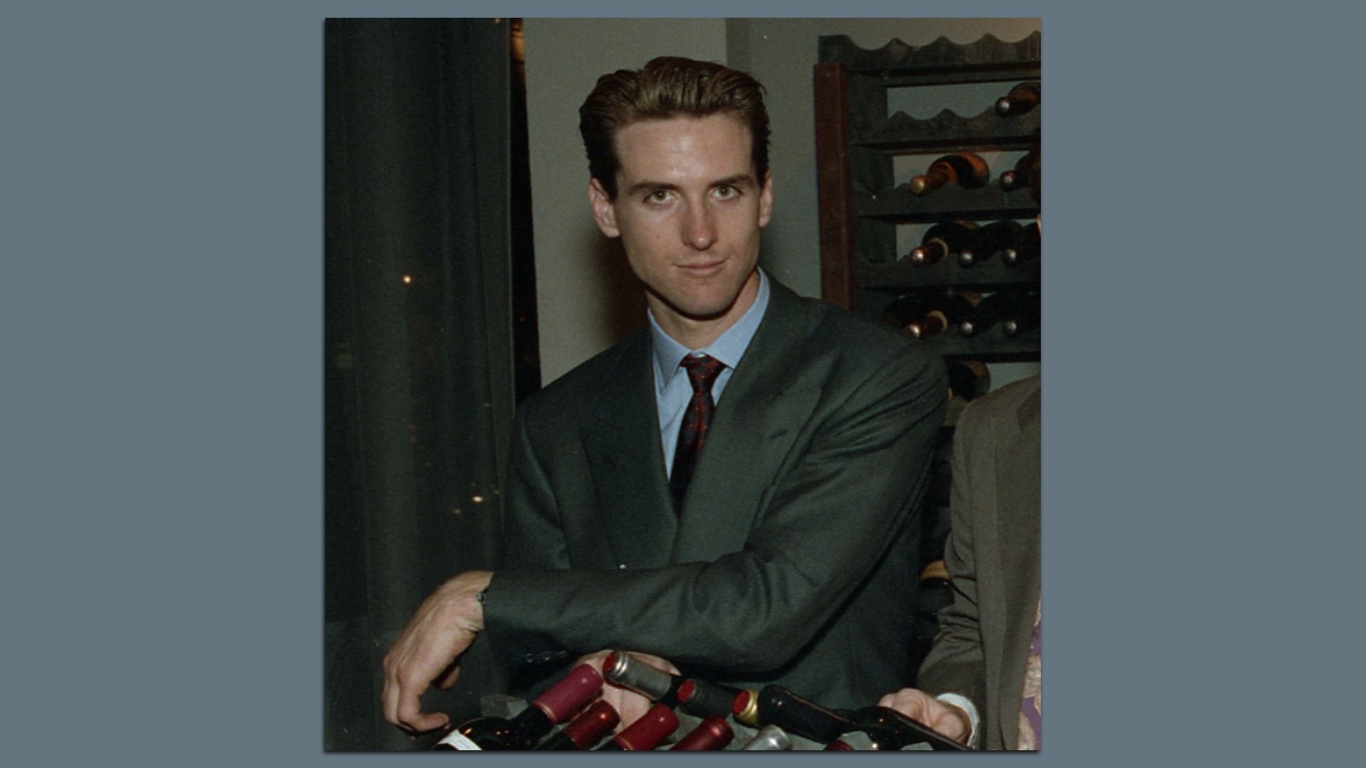 A young Gavin Newsom poses in front of bottles of wine.
