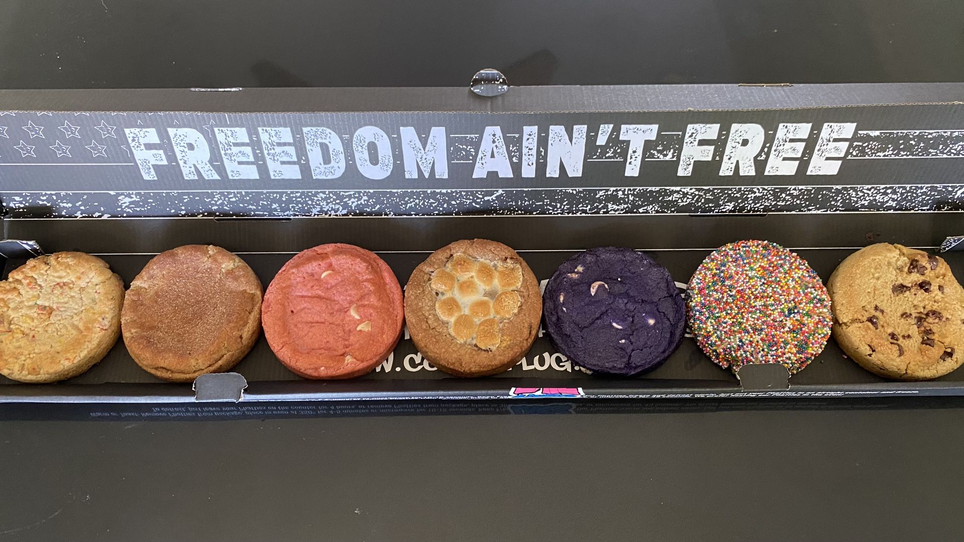 A horizontal box containing seven cookies lined up side by side. 