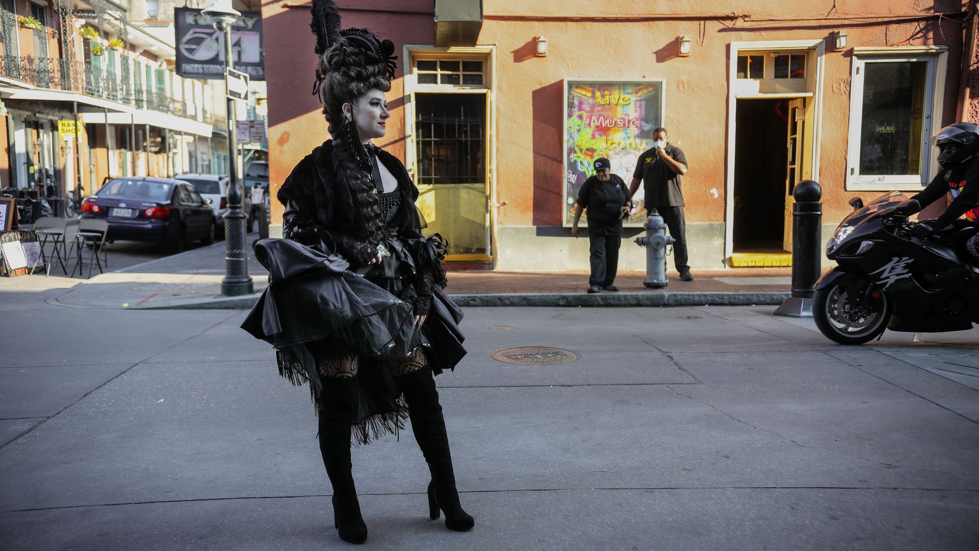 A woman in a spooky black costume and wig stands on a French Quarter streetcorner.