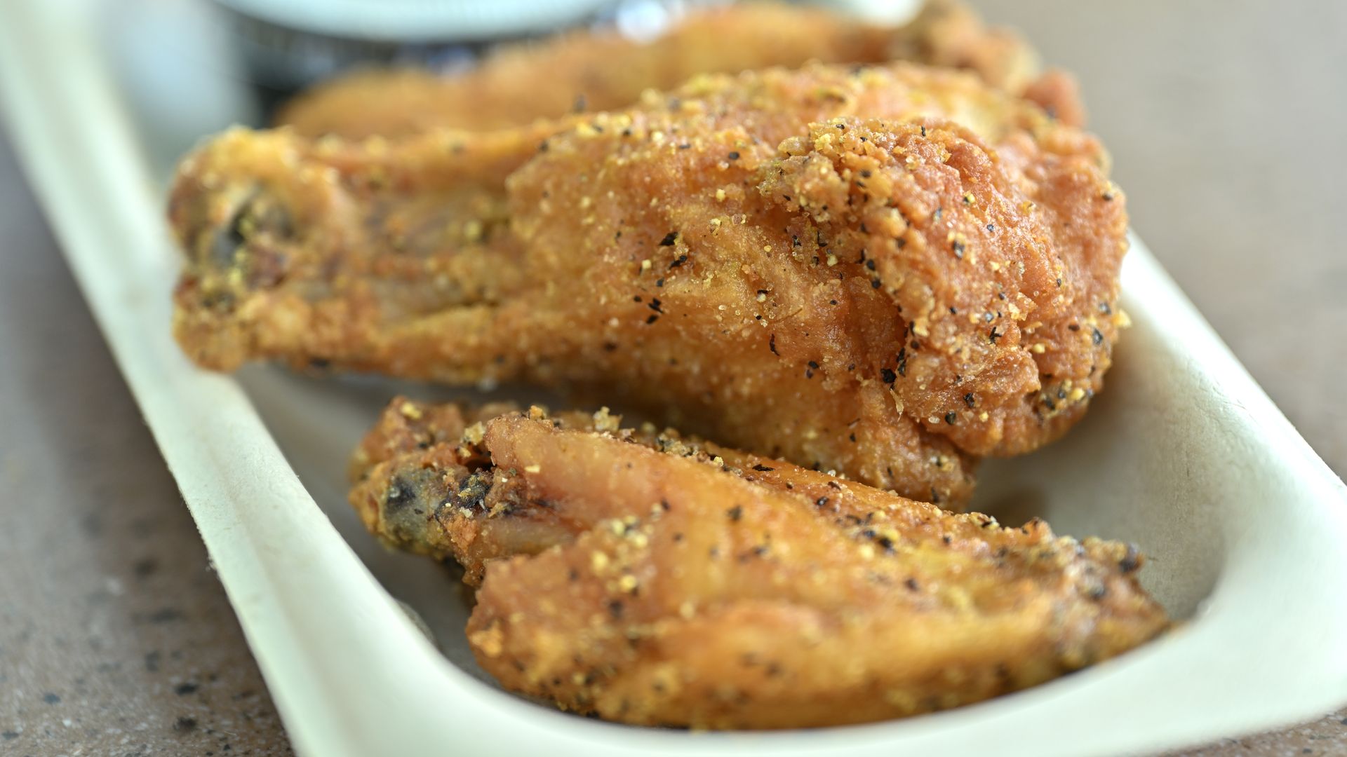 Three chicken wings sit on a narrow white serving dish, with a small container of dipping sauce in the background.