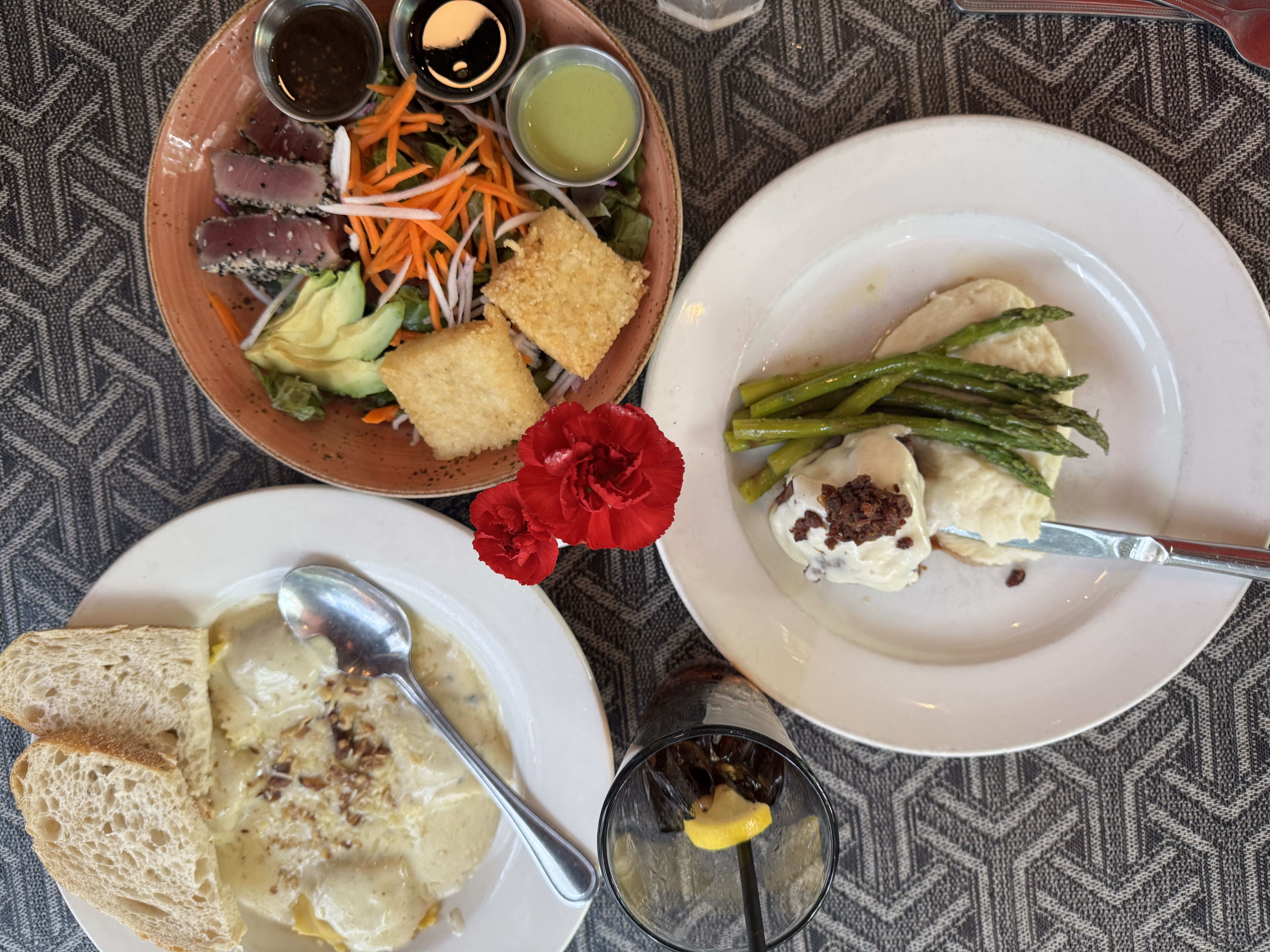 A top-down view of a meal with three plates of food on a geometric-patterned tablecloth. 