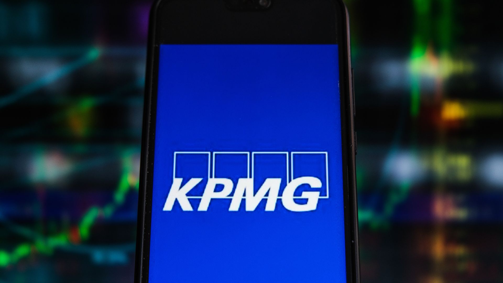 A smart phone is illuminated with the KPMG logo in white letters against a blue background.
