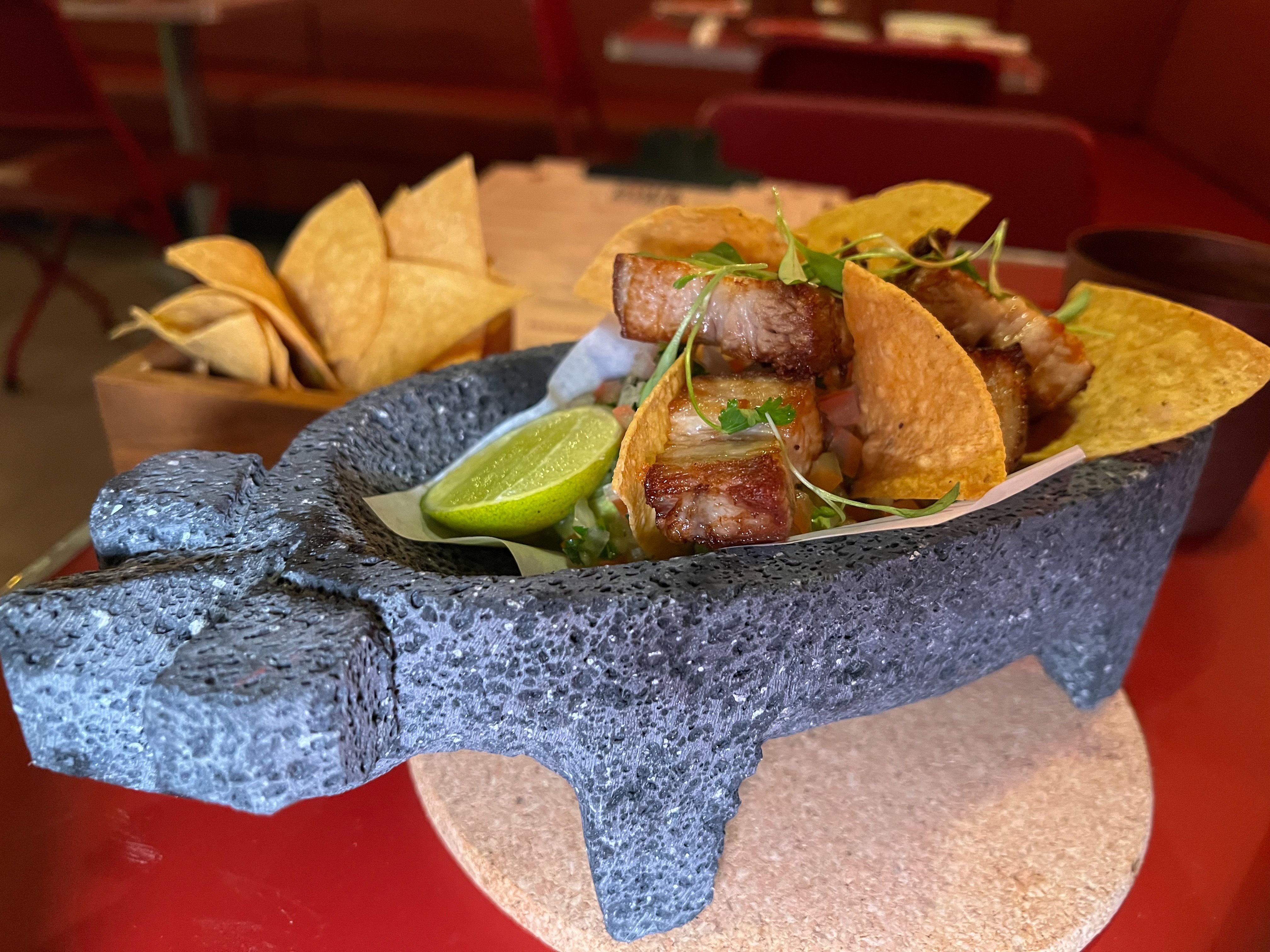 A pig-shaped brick bowl is filled with meat, chips and a lime. 