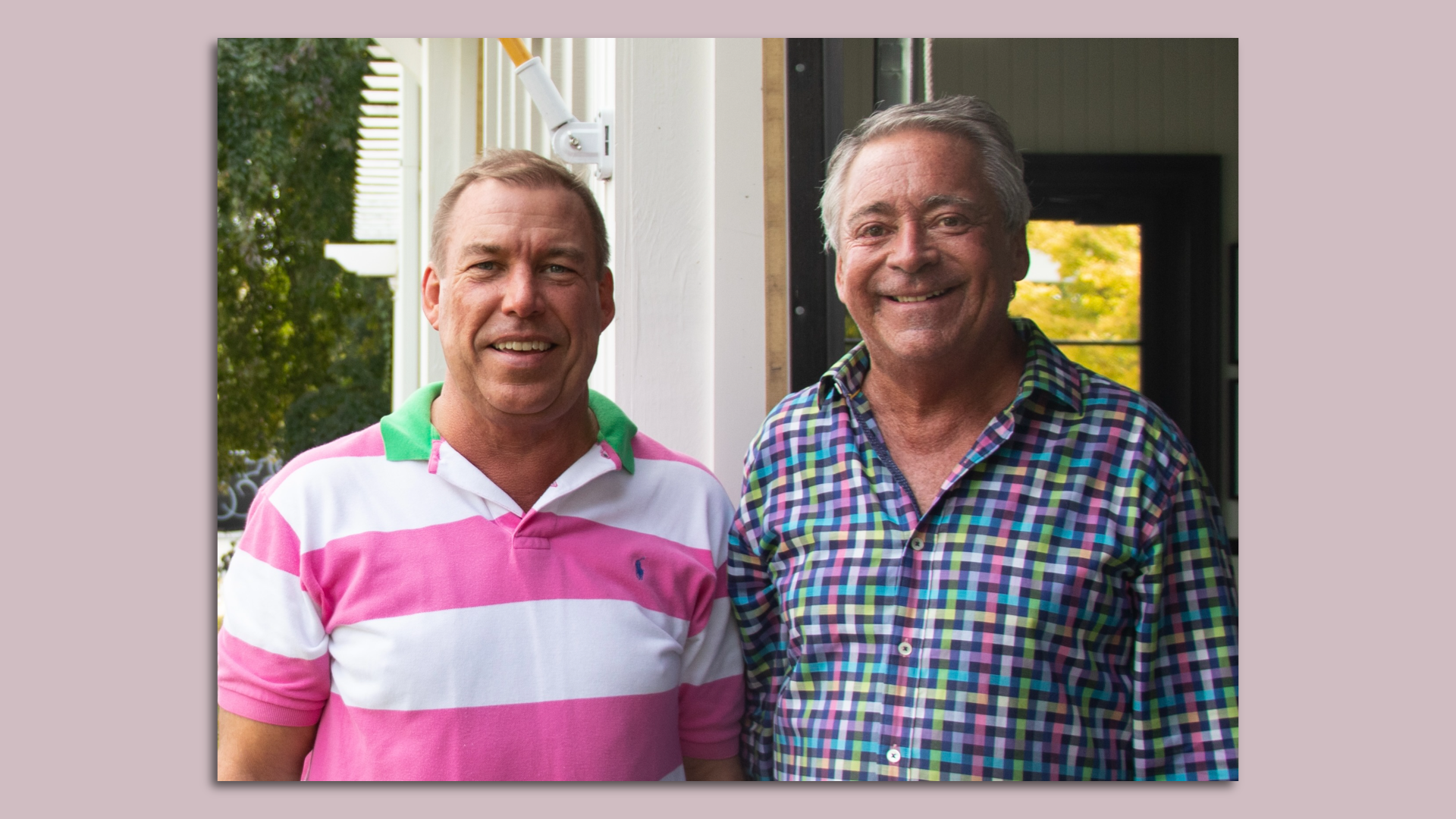 A person wearing a white and pink shirt with a green collar poses with an individual wearing a blue, yellow and violet button up shirt.