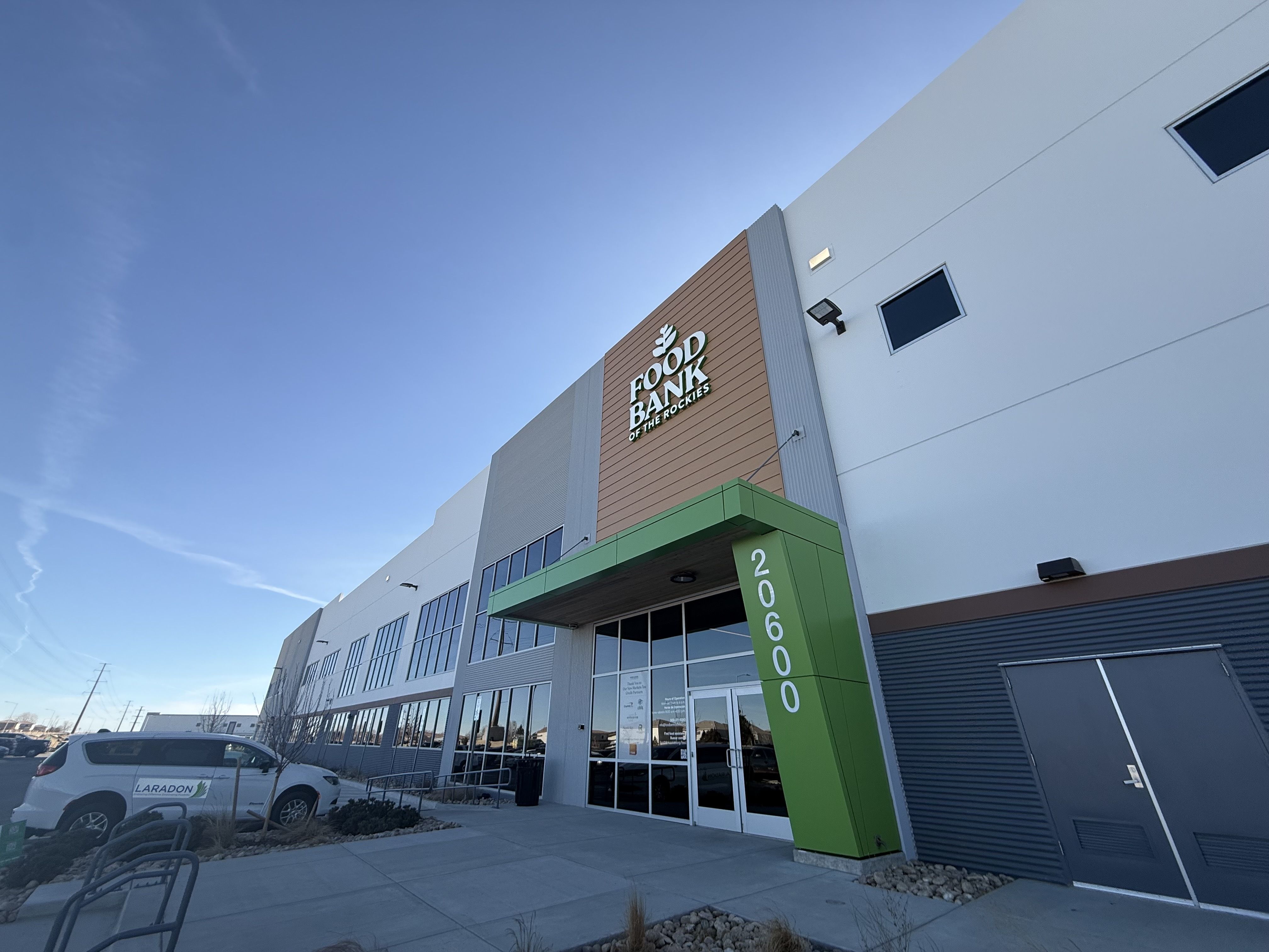 Exterior of a modern building with a green entryway marked 20600 and a sign reading Food Bank of the Rockies against a clear blue sky.