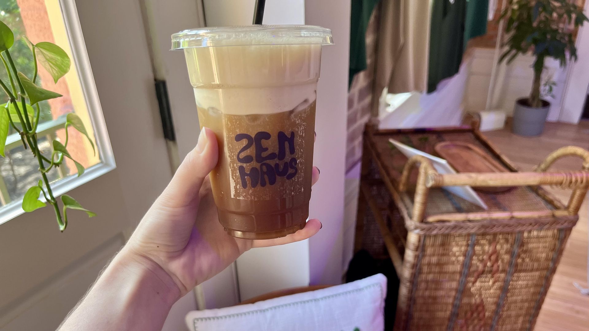 An arm outstretched holding a plastic coffee cup filled with brown liquid. 