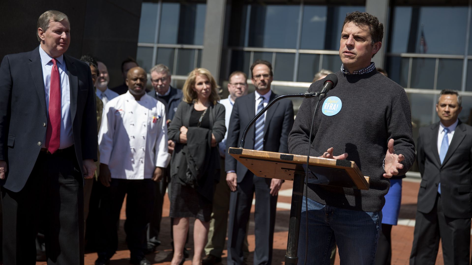 Bill Oesterle speaks at an outdoor lectern in 2015 surrounded by other Indianapolis leaders.