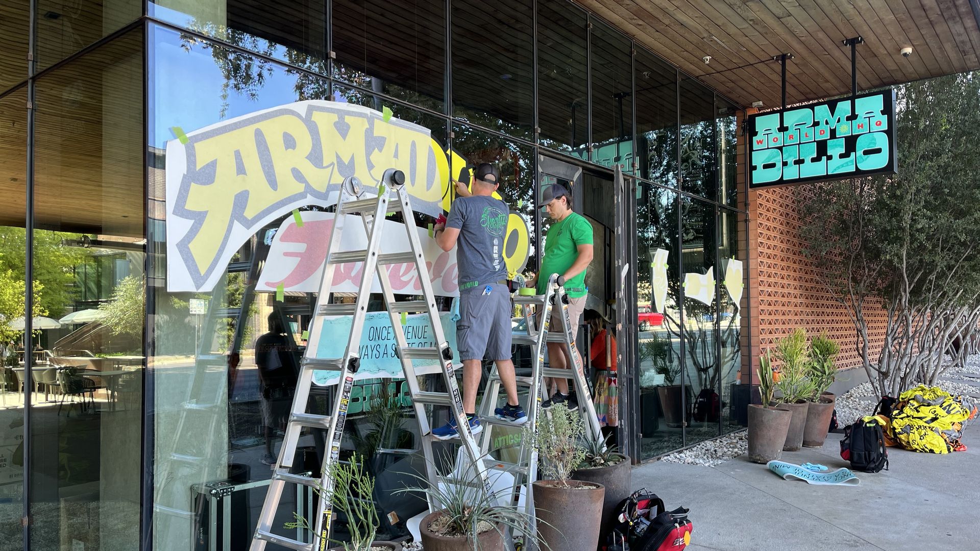 Two workers on ladders put signs out front of the new Armadillo store.