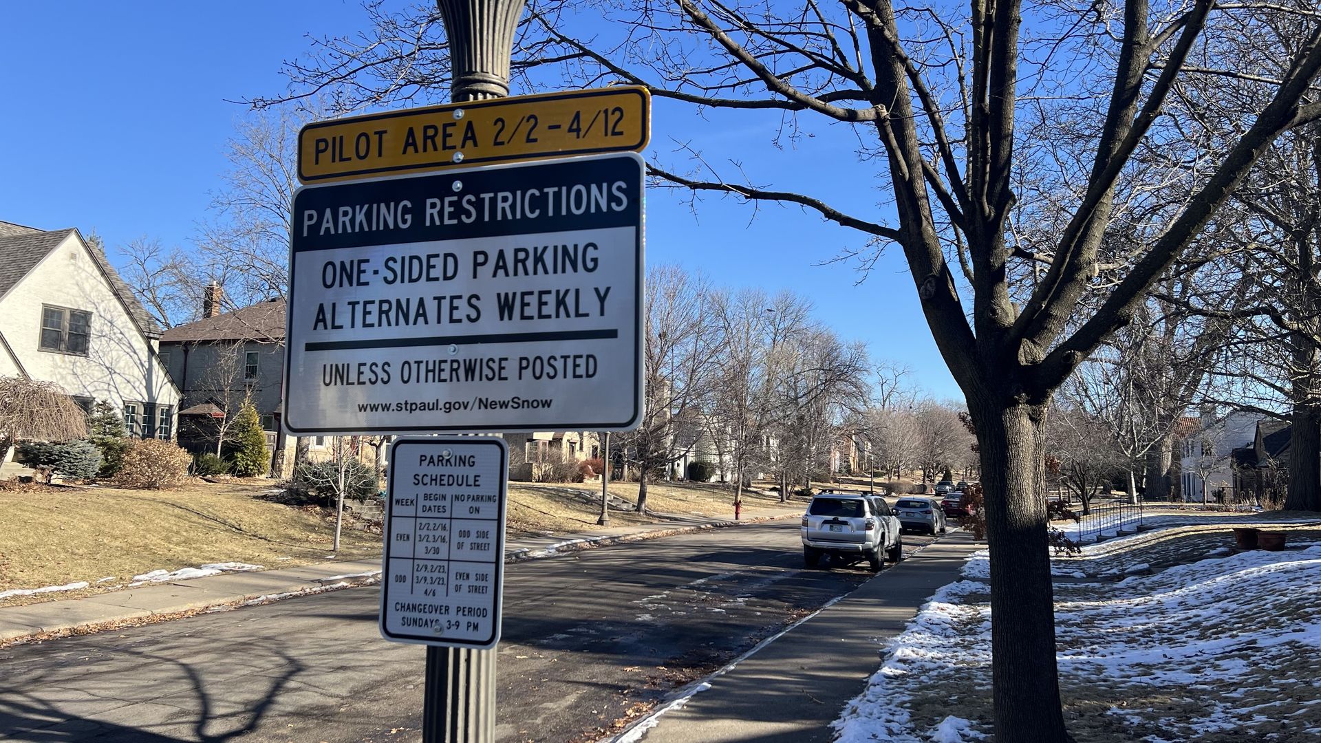 A parking restriction sign in a neighborhood on a straight residential street that reads: "Pilot Area, 2/2-4/12 - Parking Restrictions - One-Sided Parking Alternates Weekly"