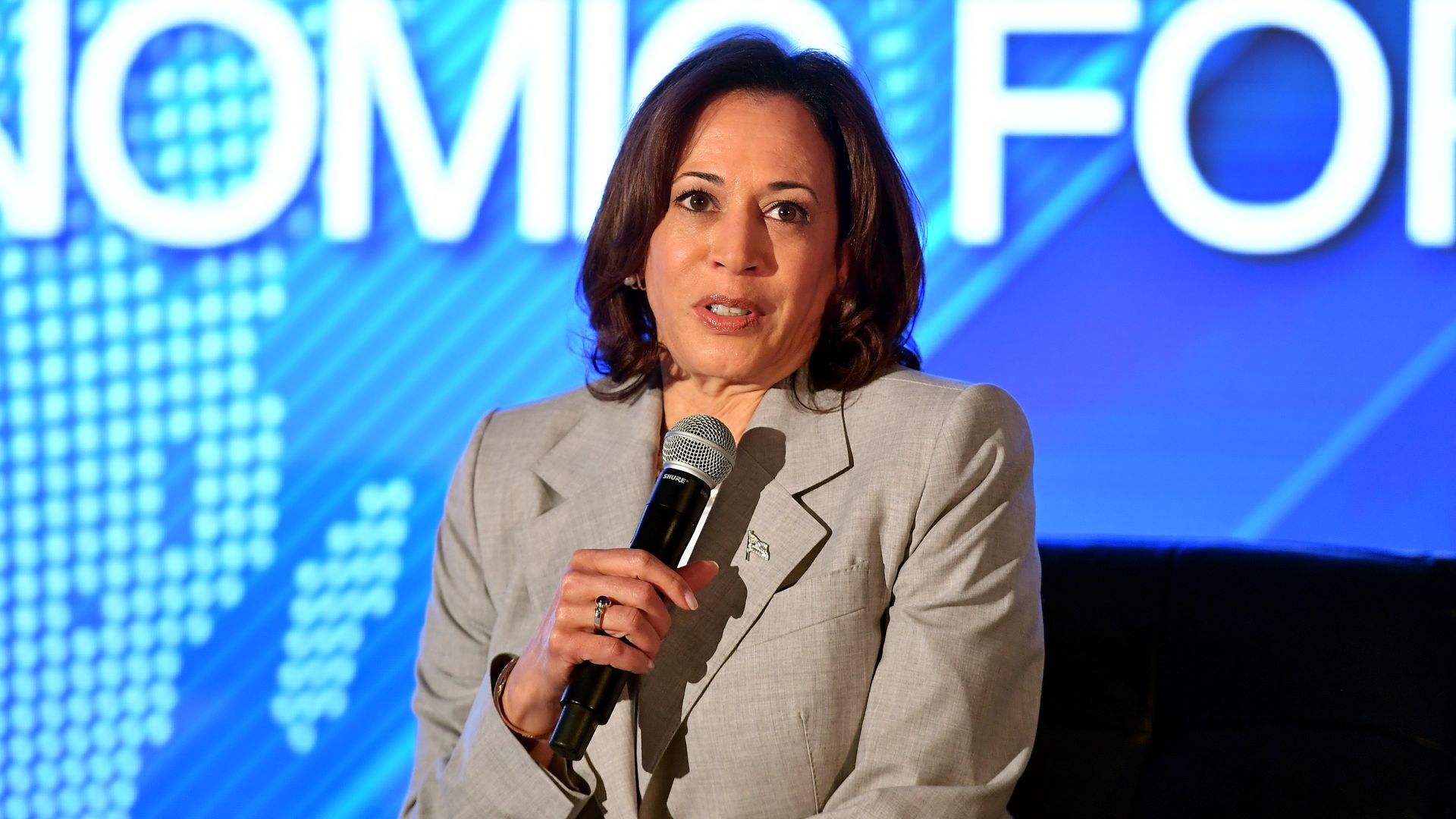 Photo shows VP Kamala Harris, wearing a suit and holding a microphone, on stage at the Global Black Economic Forum.