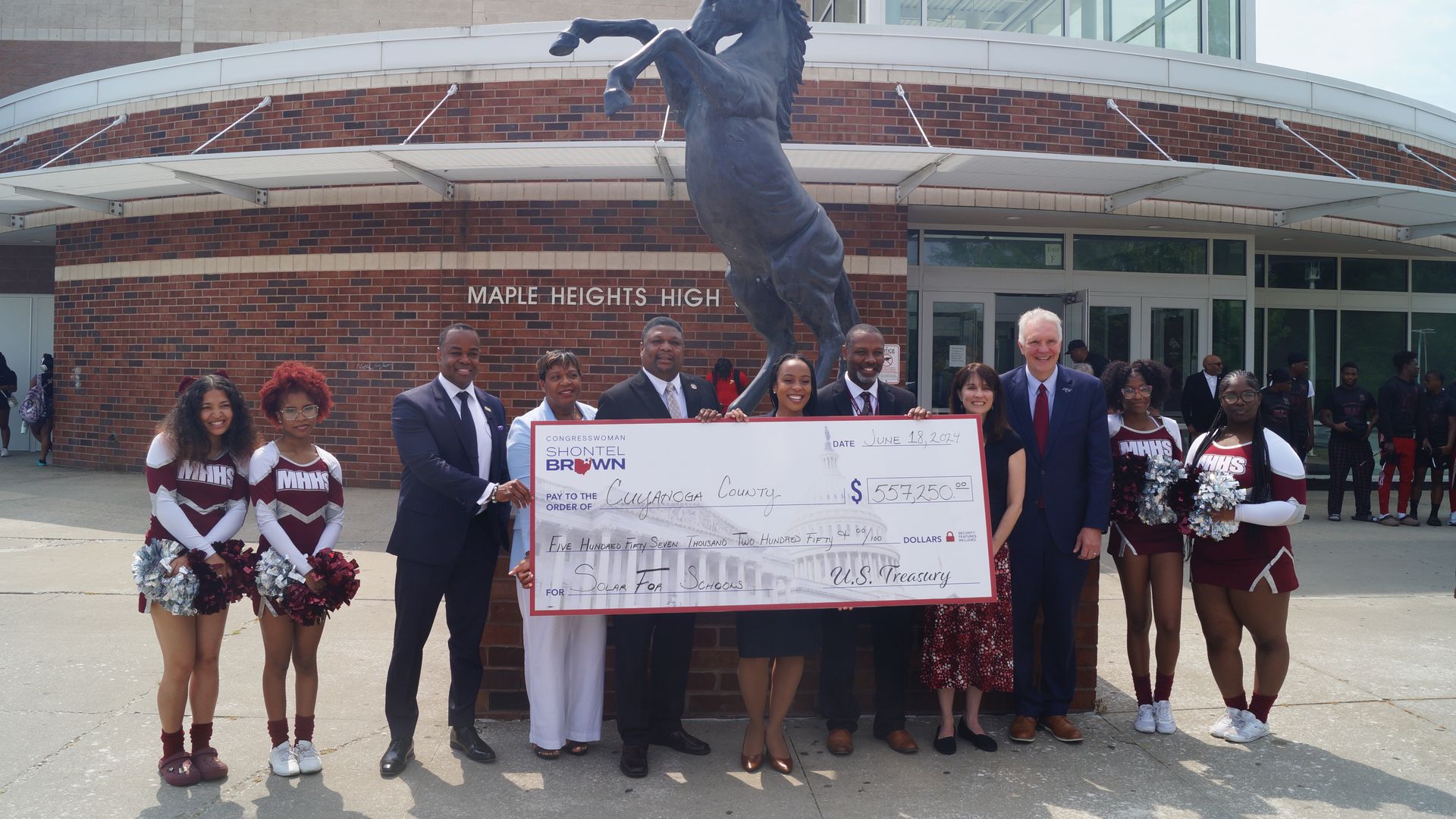 Officials hold a check for $557,000 in front of Maple Heights High School building and statue of mustang