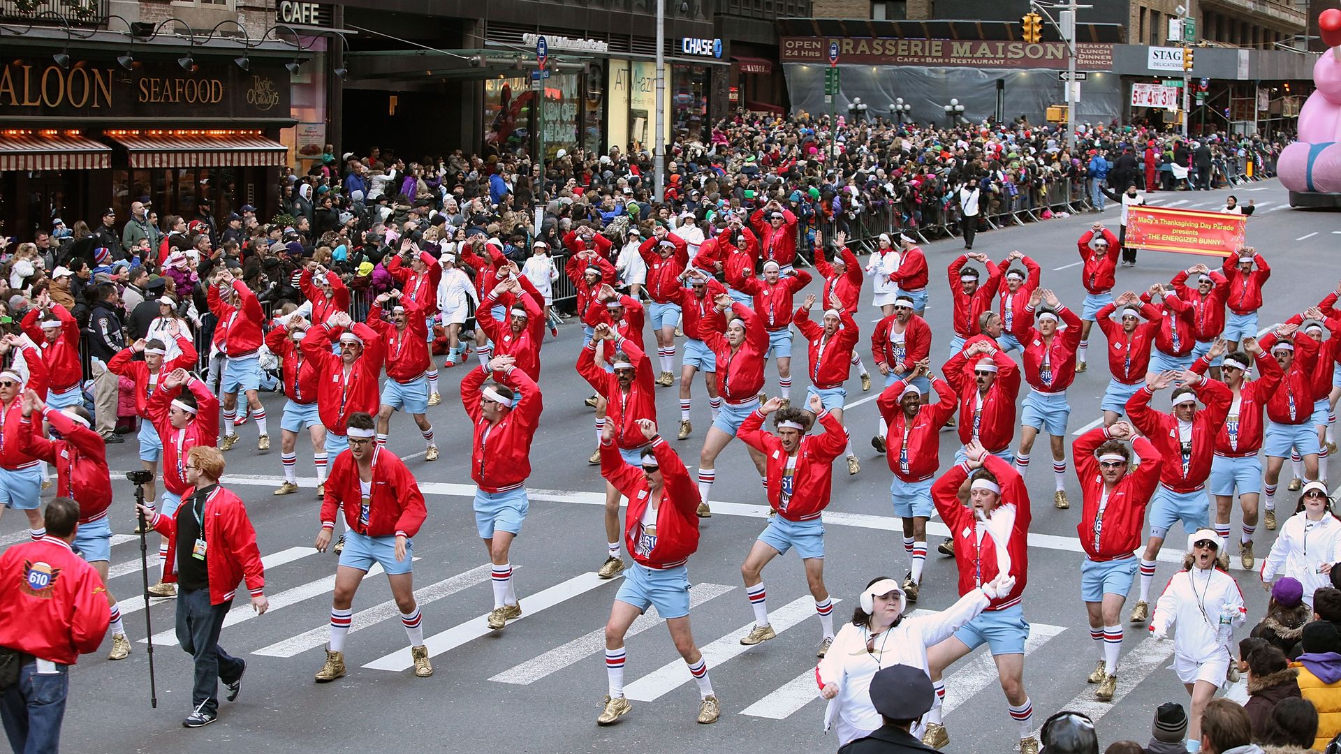 The 610 Stompers dance, mid-routine, in a photo during a parade. The dancers fill a wide avenue between crowds.