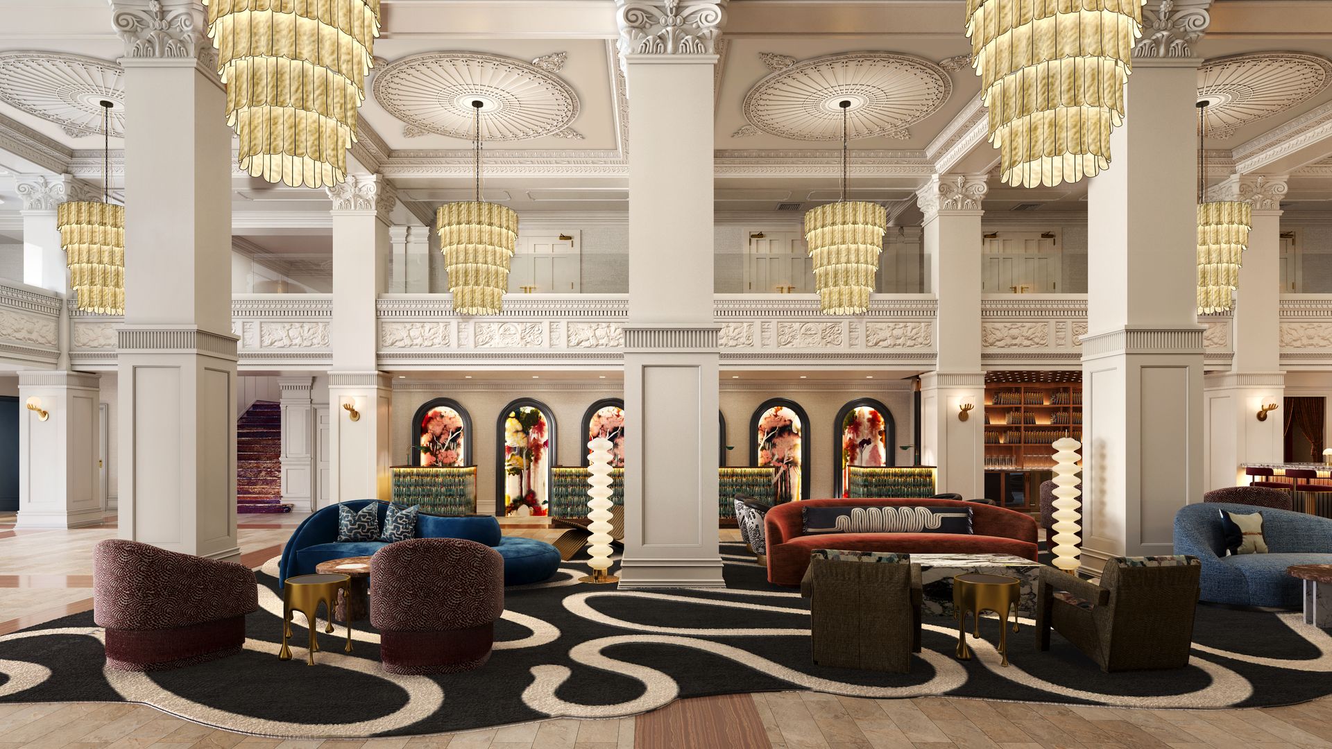 Elegant hotel lobby with white ornate columns, large layered gold chandeliers, colorful sofas and chairs on a black and white abstract rug, and floral artwork in arched niches.