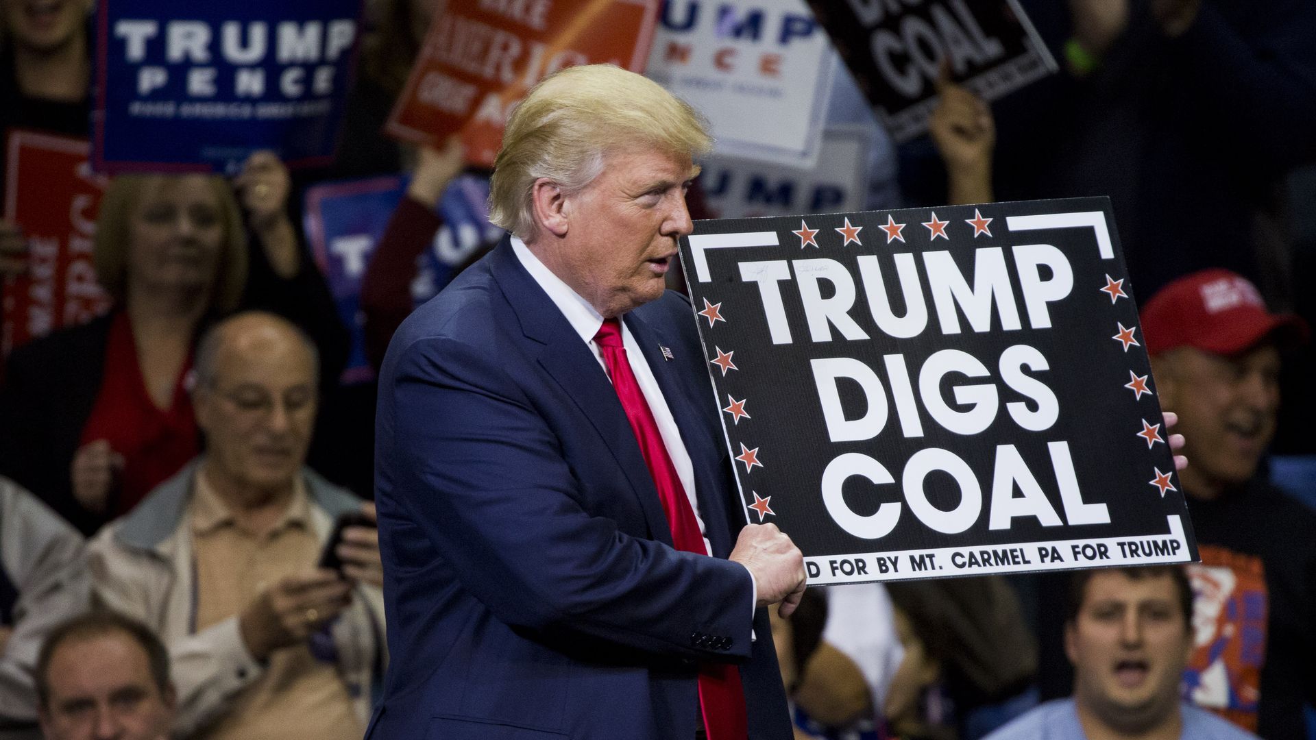 Trump at a rally holding a trump digs coal sign