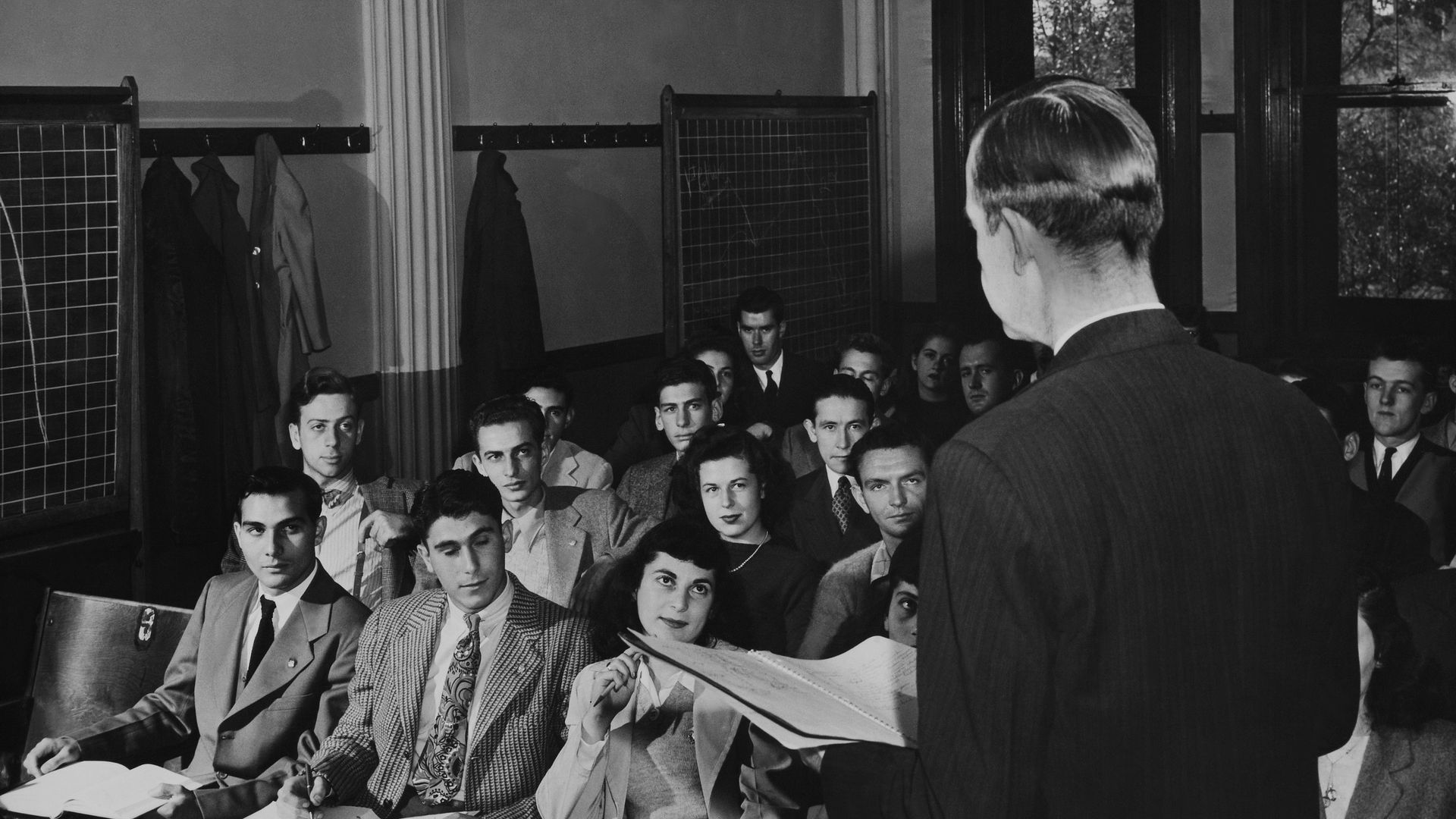 A lecturer stands before rows of students in a black and white photo