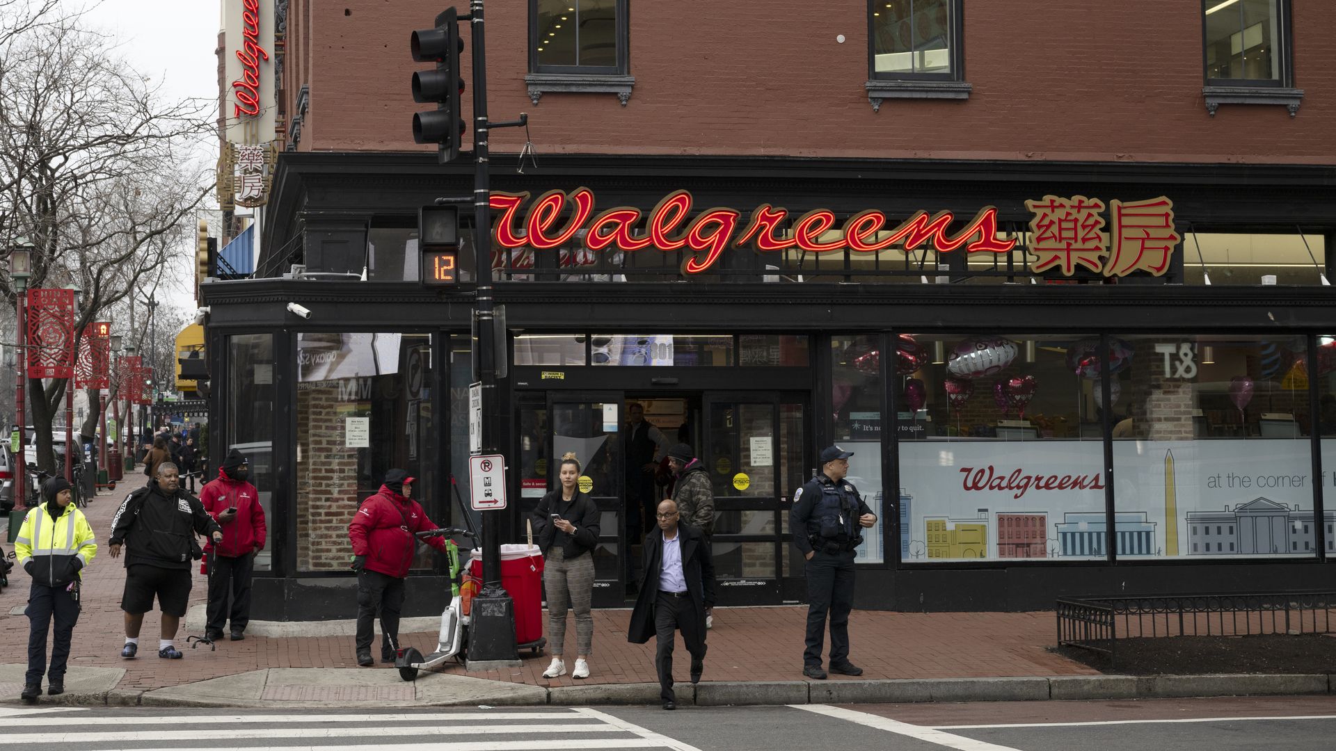 People stand on a street corner outside a building with a Walgreens sign.