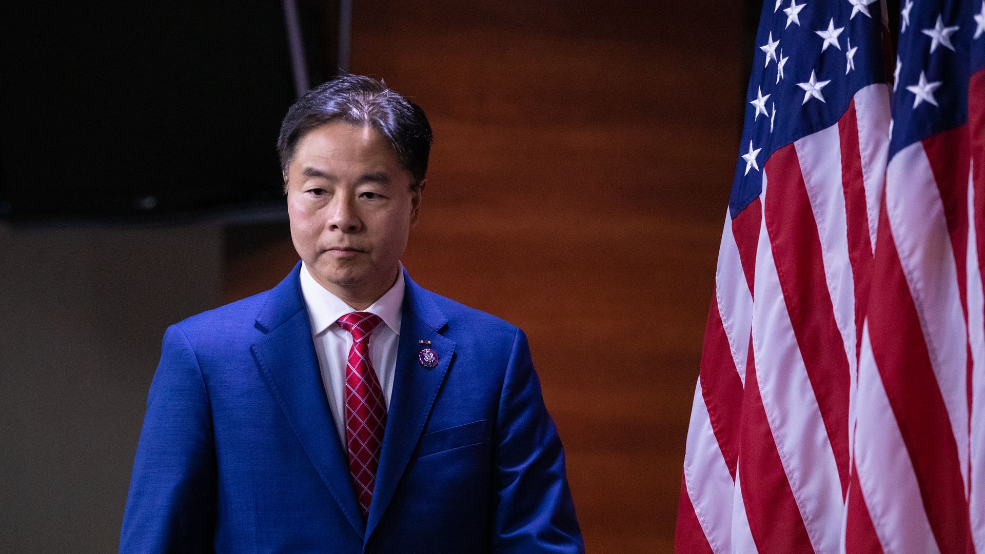 Rep. Ted Lieu is pictured in a blue suit next to a US flag