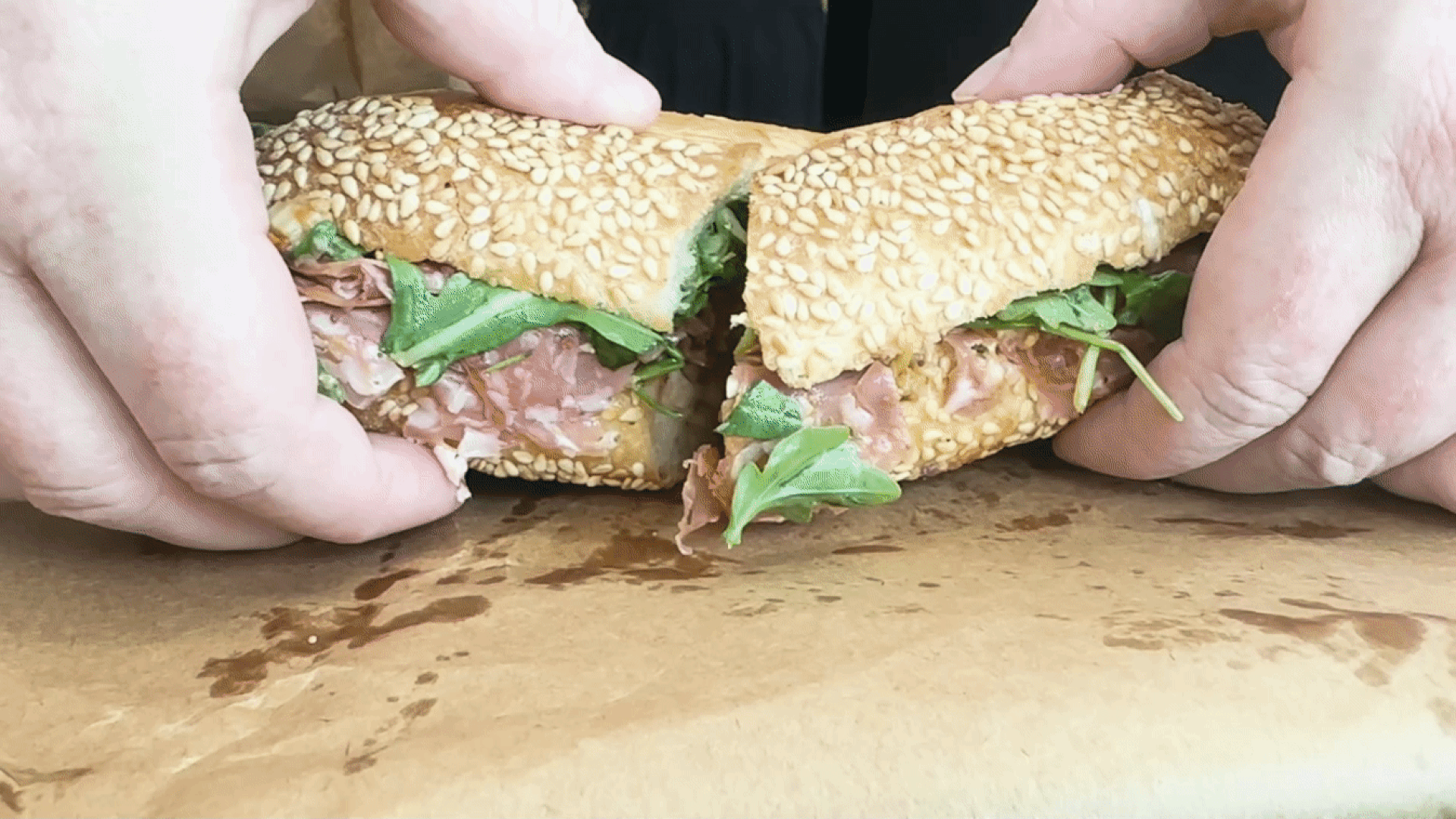 Two hands pull apart a deli sandwich on seeded bread.