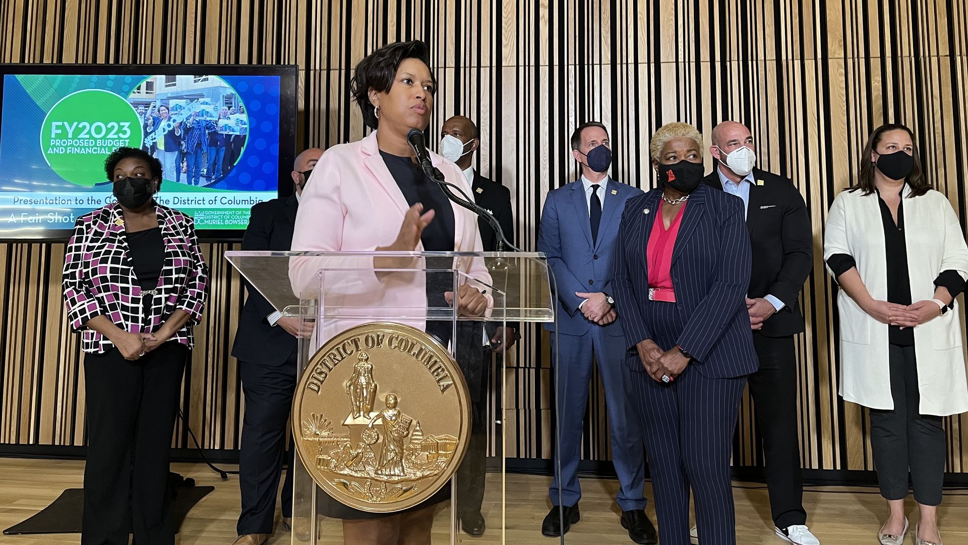 Mayor Muriel Bowser stands before a podium with her cabinet behind her