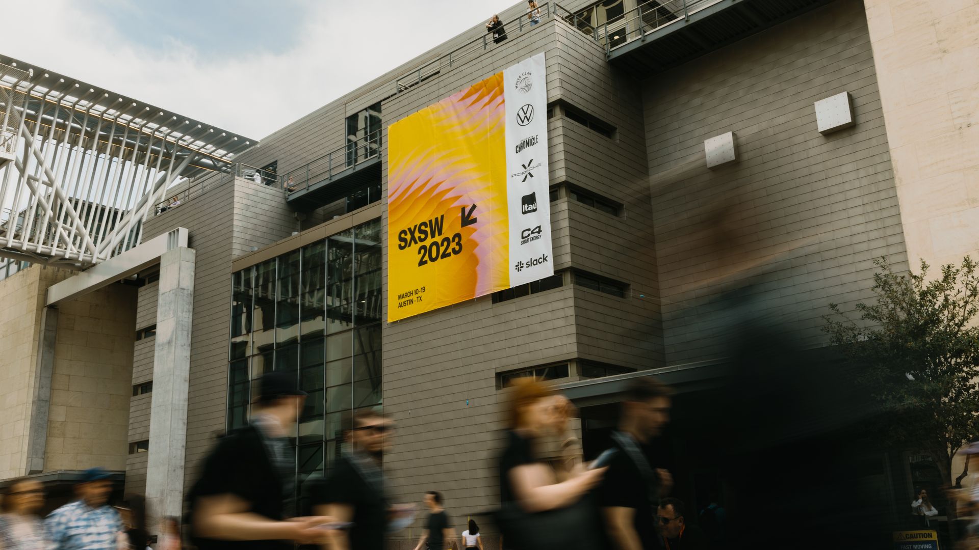 Attendees stroll by the Austin Convention Center and SXSW banners.